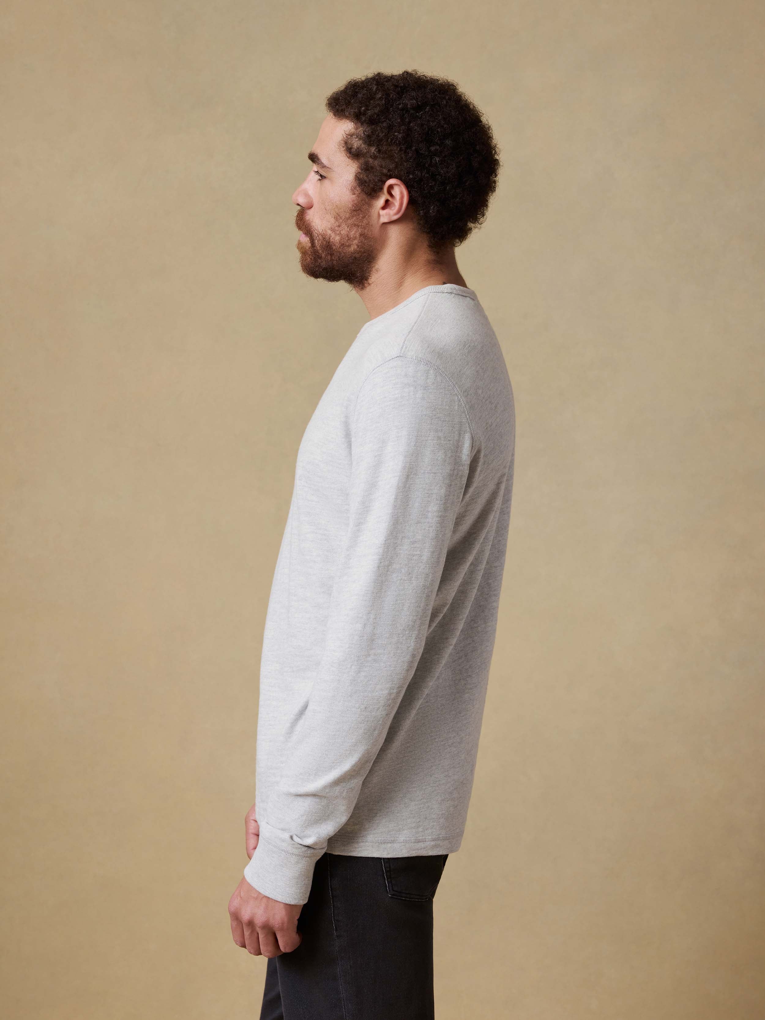 Man wearing a light gray long sleeve shirt and dark pants against a beige background