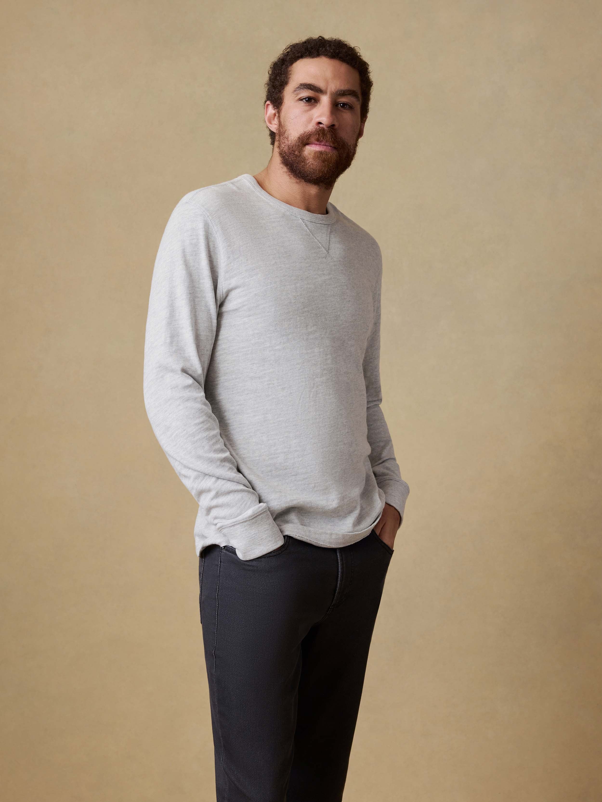 Man wearing a light gray long sleeve shirt and dark pants against a beige background