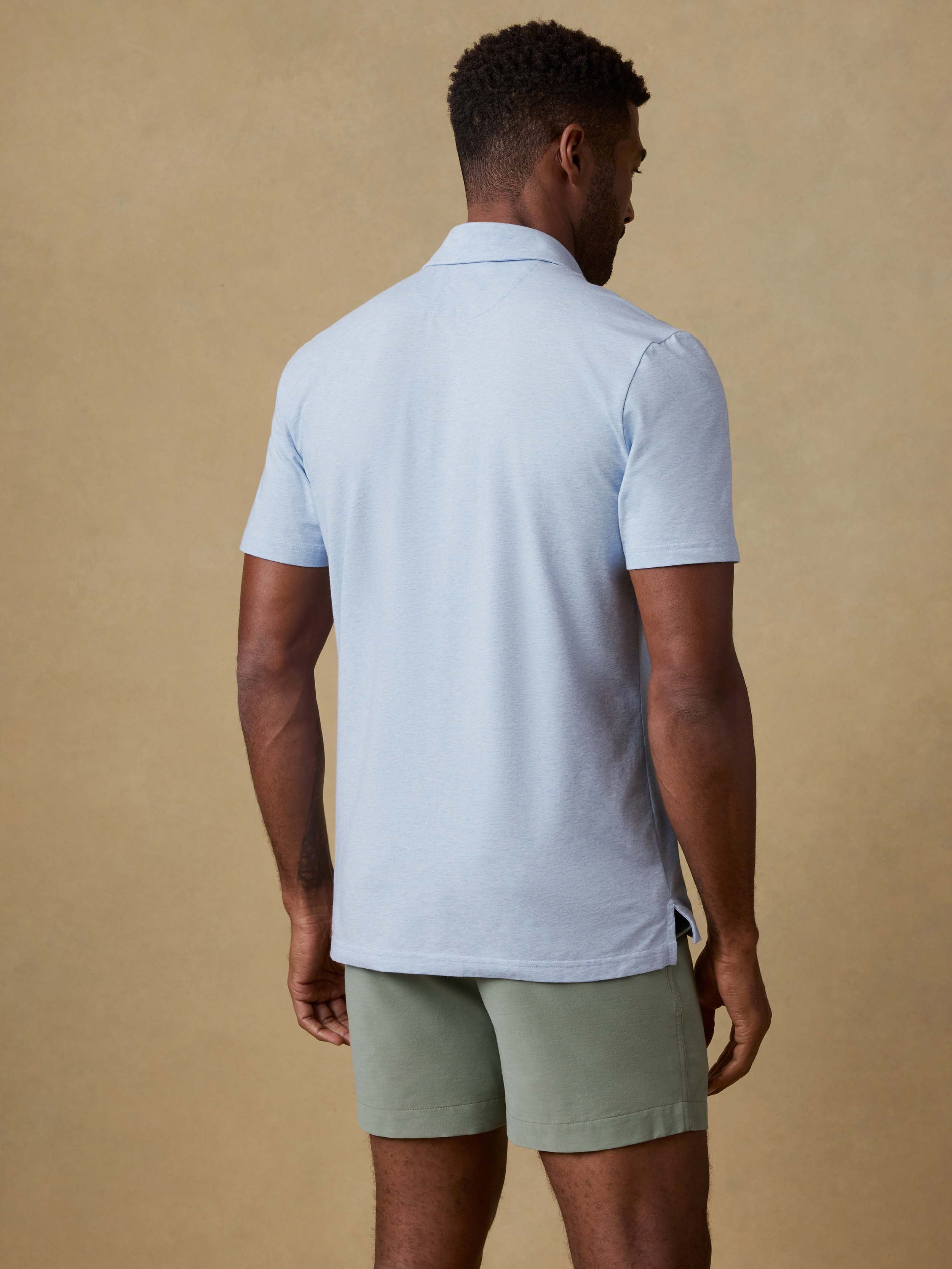 Back view of a man wearing a light blue polo shirt and green shorts against a beige background