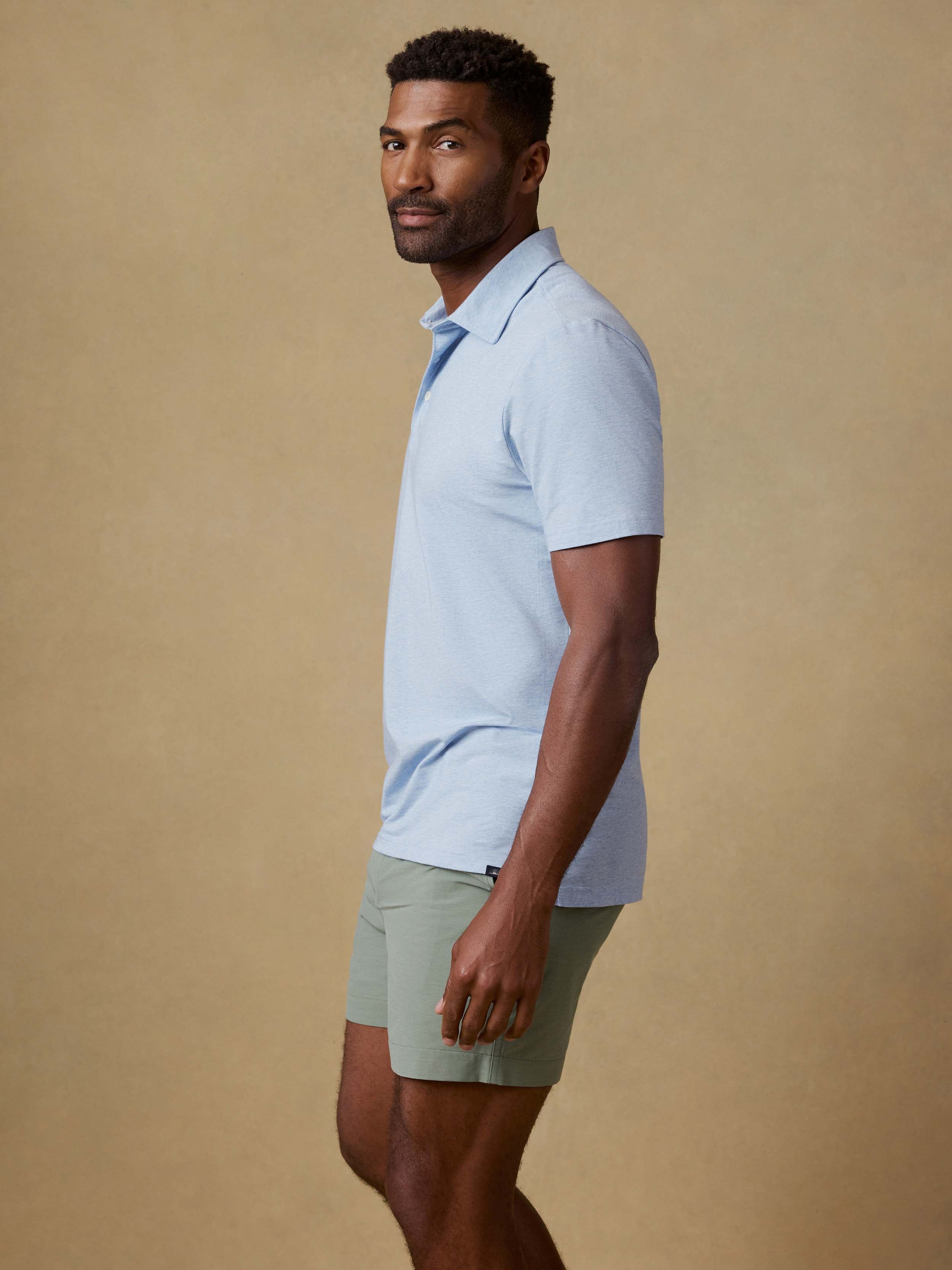 Man wearing a light blue polo shirt and green shorts against a beige background