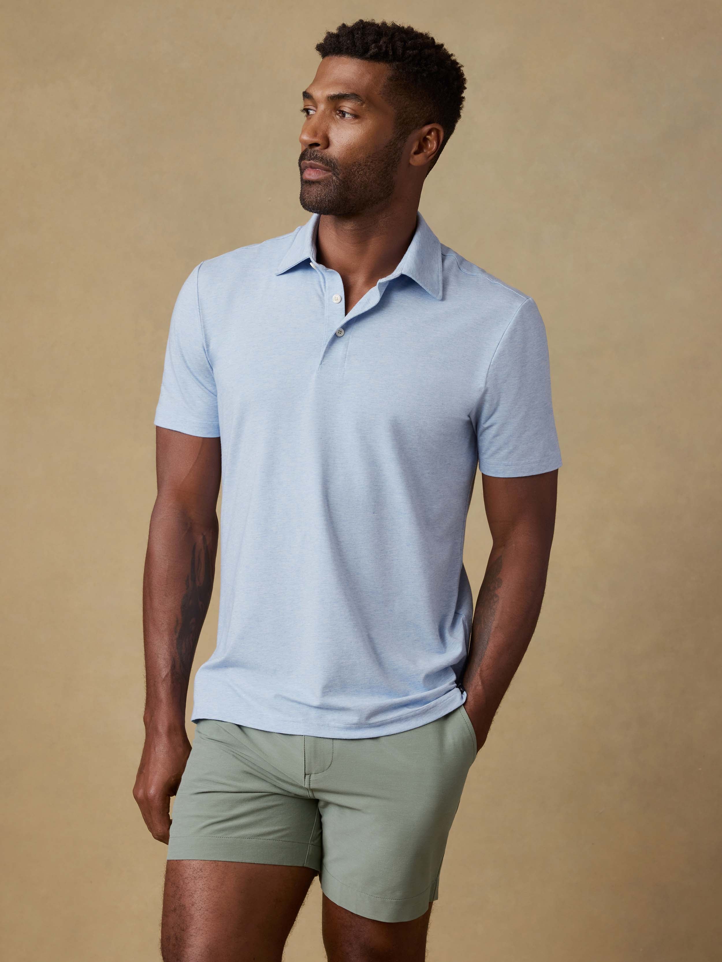 Man wearing a light blue polo shirt and green shorts against a beige background