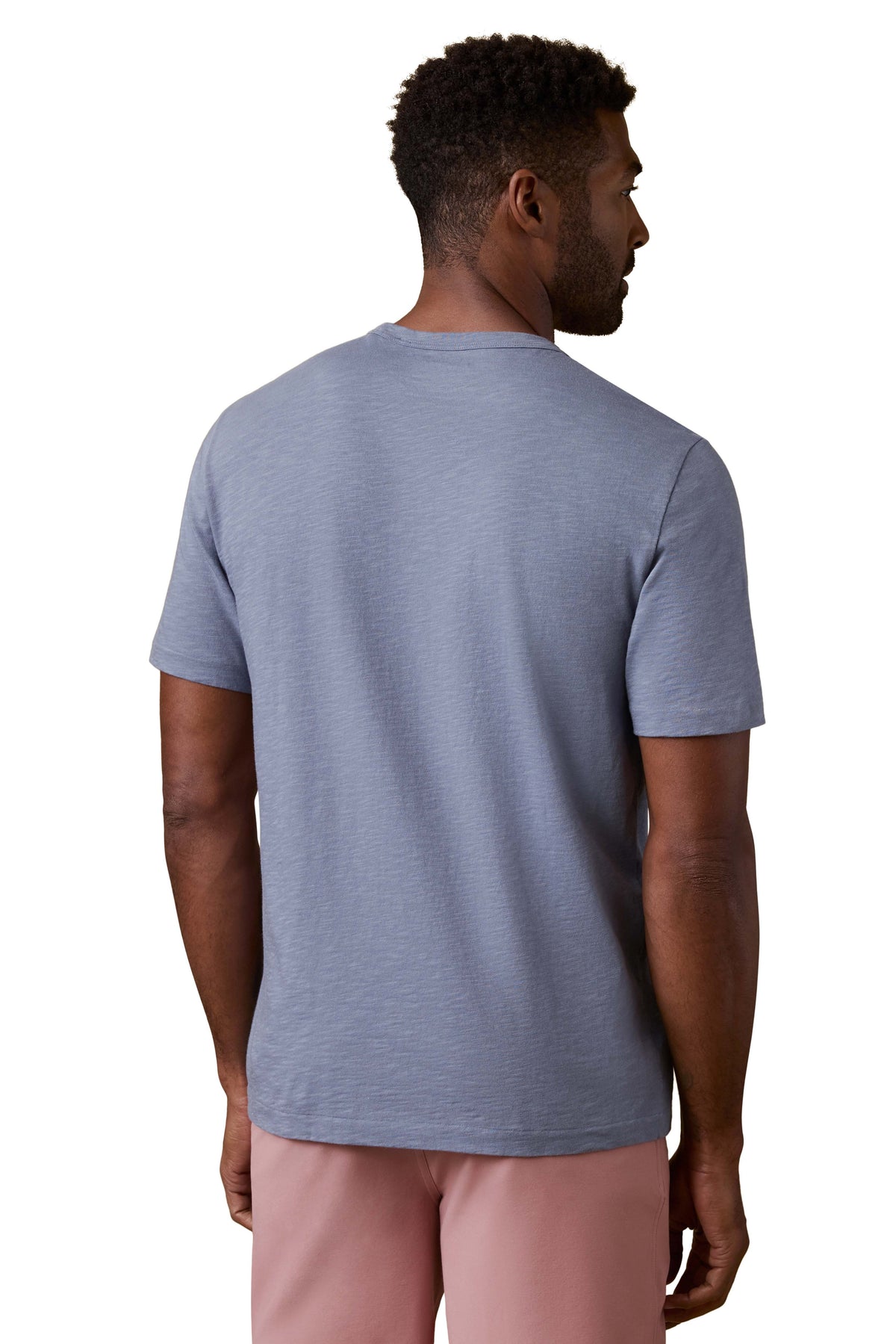 A man viewed from behind wearing a periwinkle tee and pink shorts, image 3 of 3