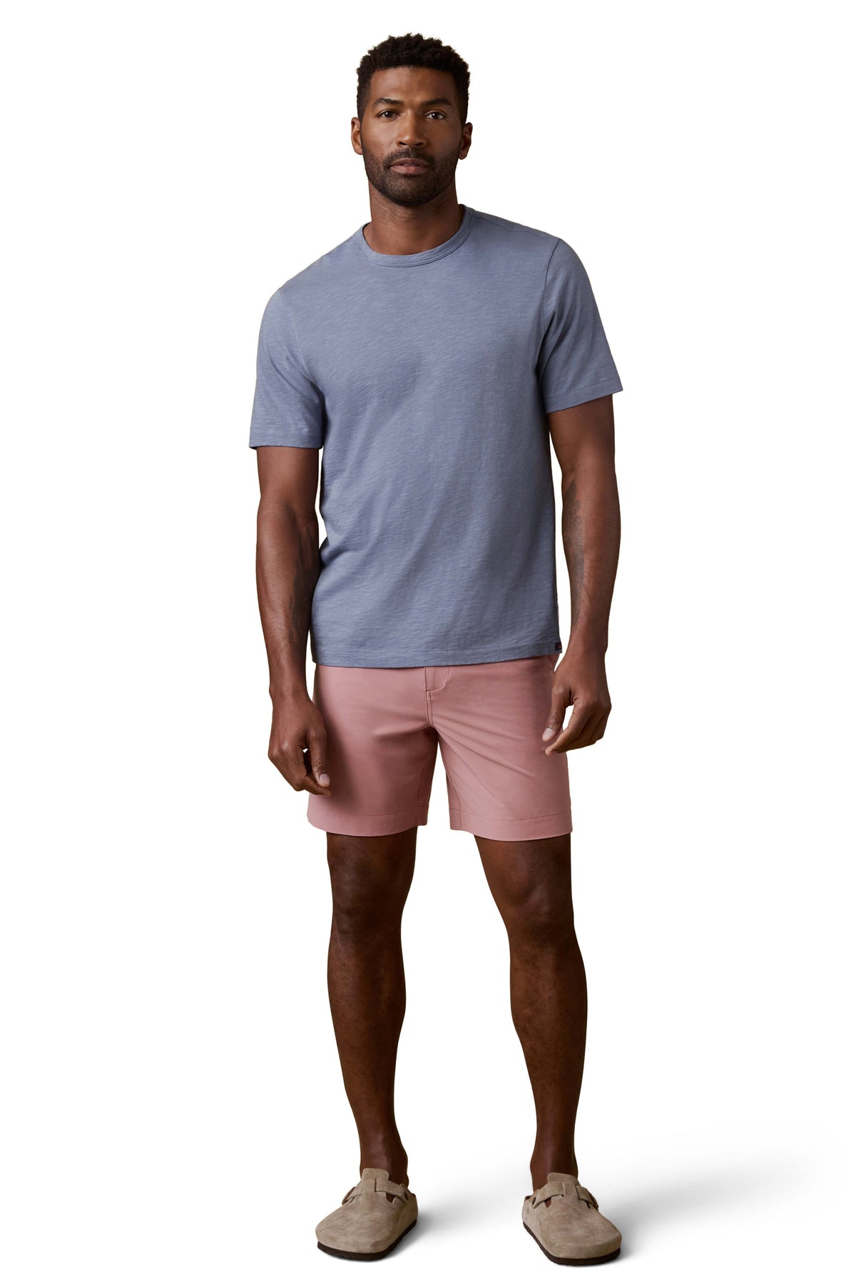 A man wearing a periwinkle tee, pink shorts, and birkenstocks, image 2 of 3