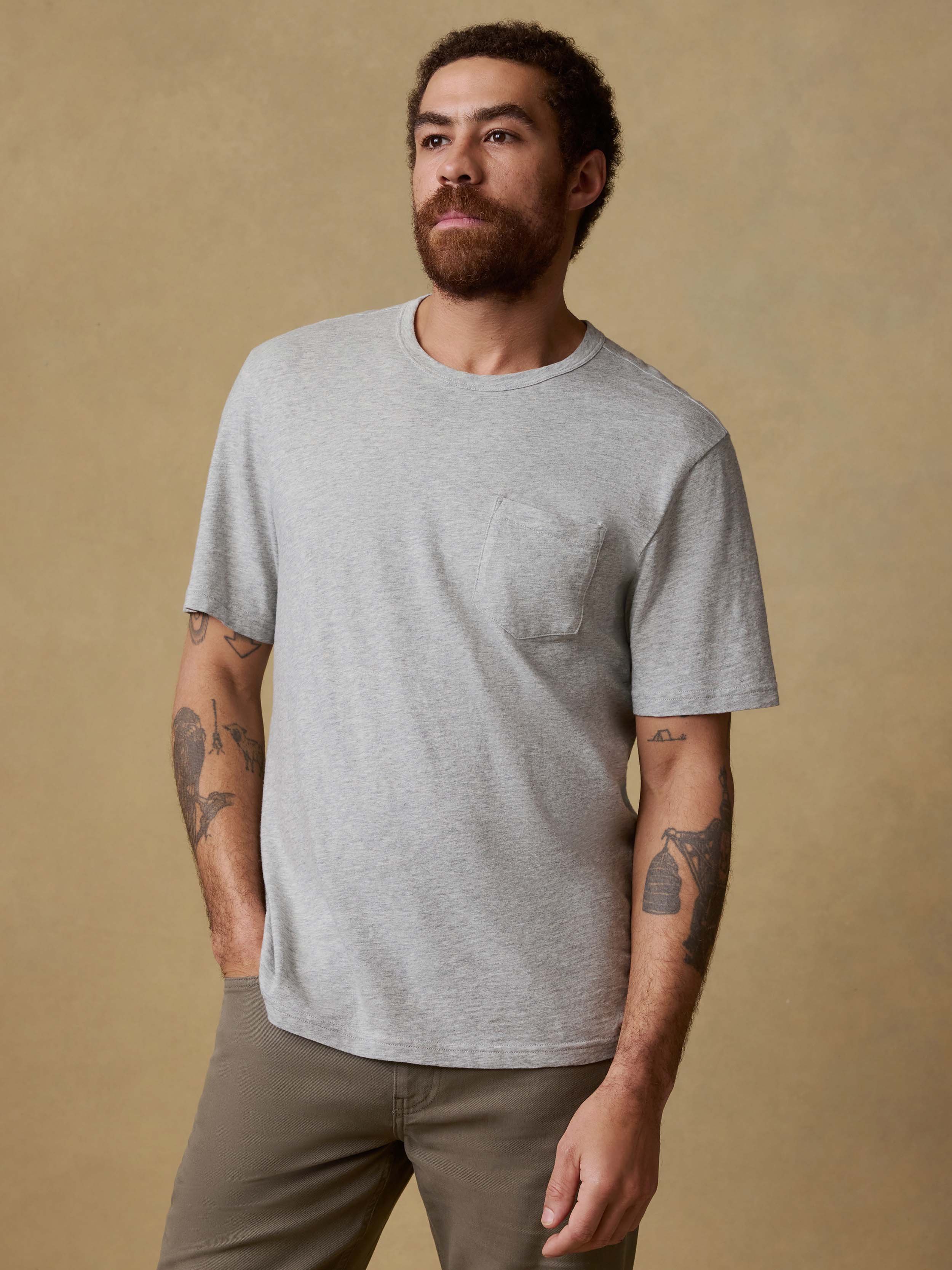 Man wearing a gray t-shirt and brown pants against a beige background