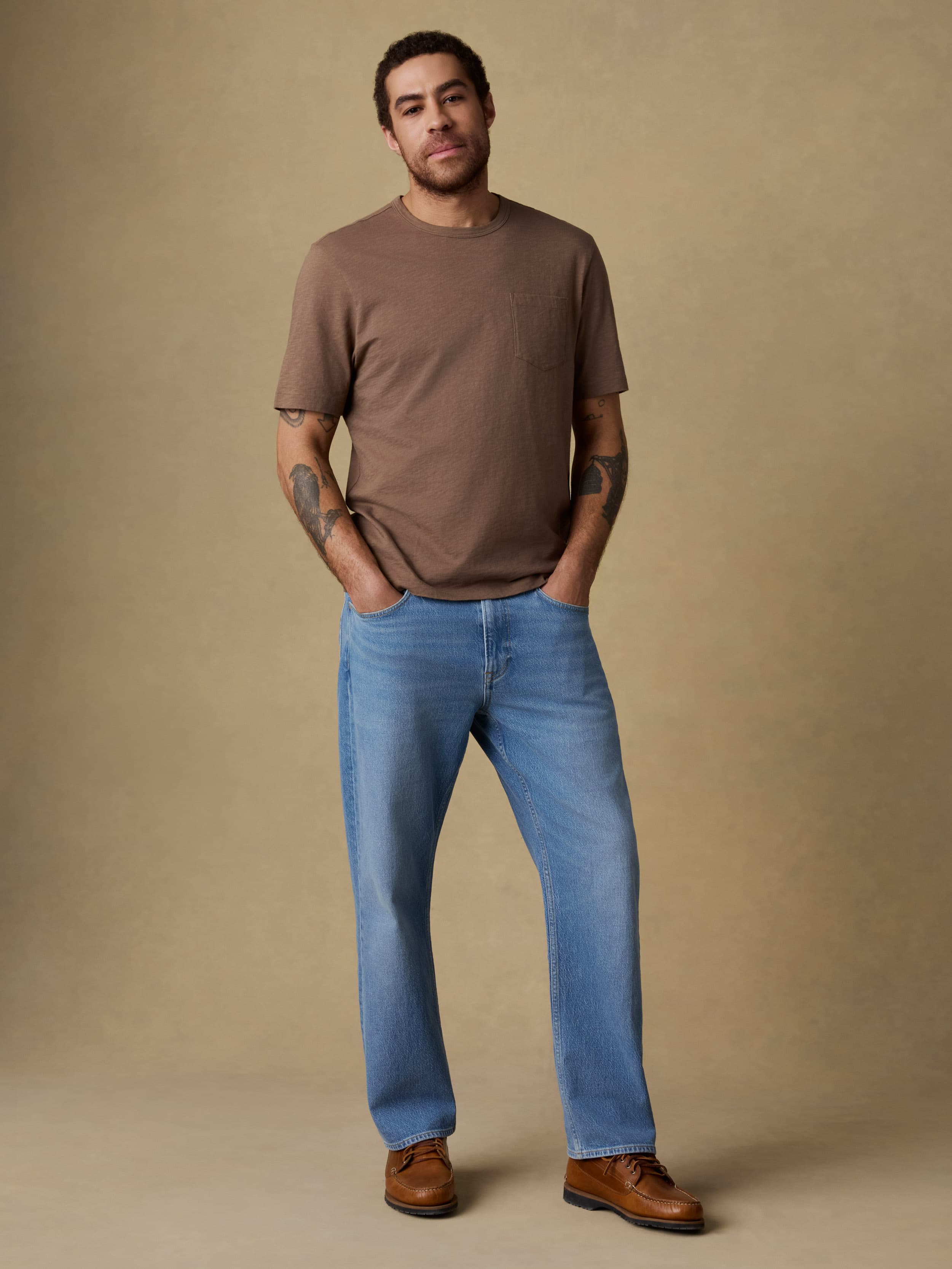 Man wearing a brown short sleeve t-shirt and blue jeans against a beige background