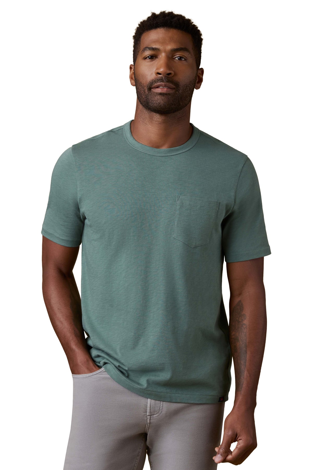 A man wearing a green tee and grey pants, image 1 of 3