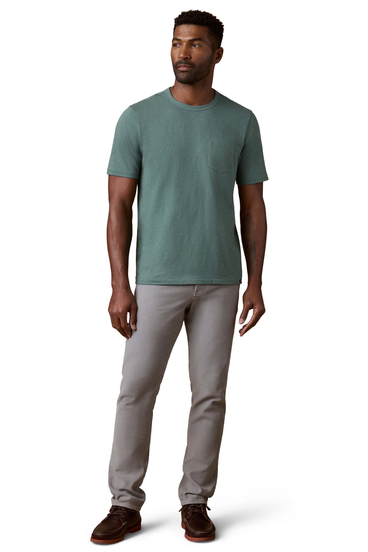 A man wearing a green tee, grey pants, and brown shoes, image 2 of 3