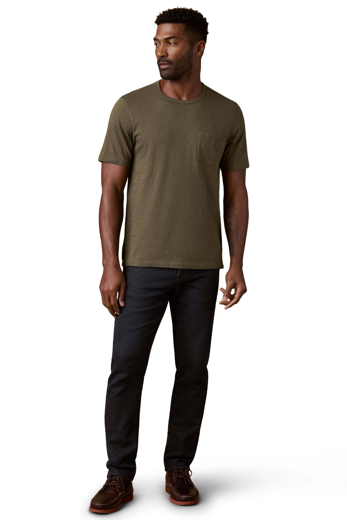 A man wearing a green tee, black jeans, and brown shoes, image 2 of 3