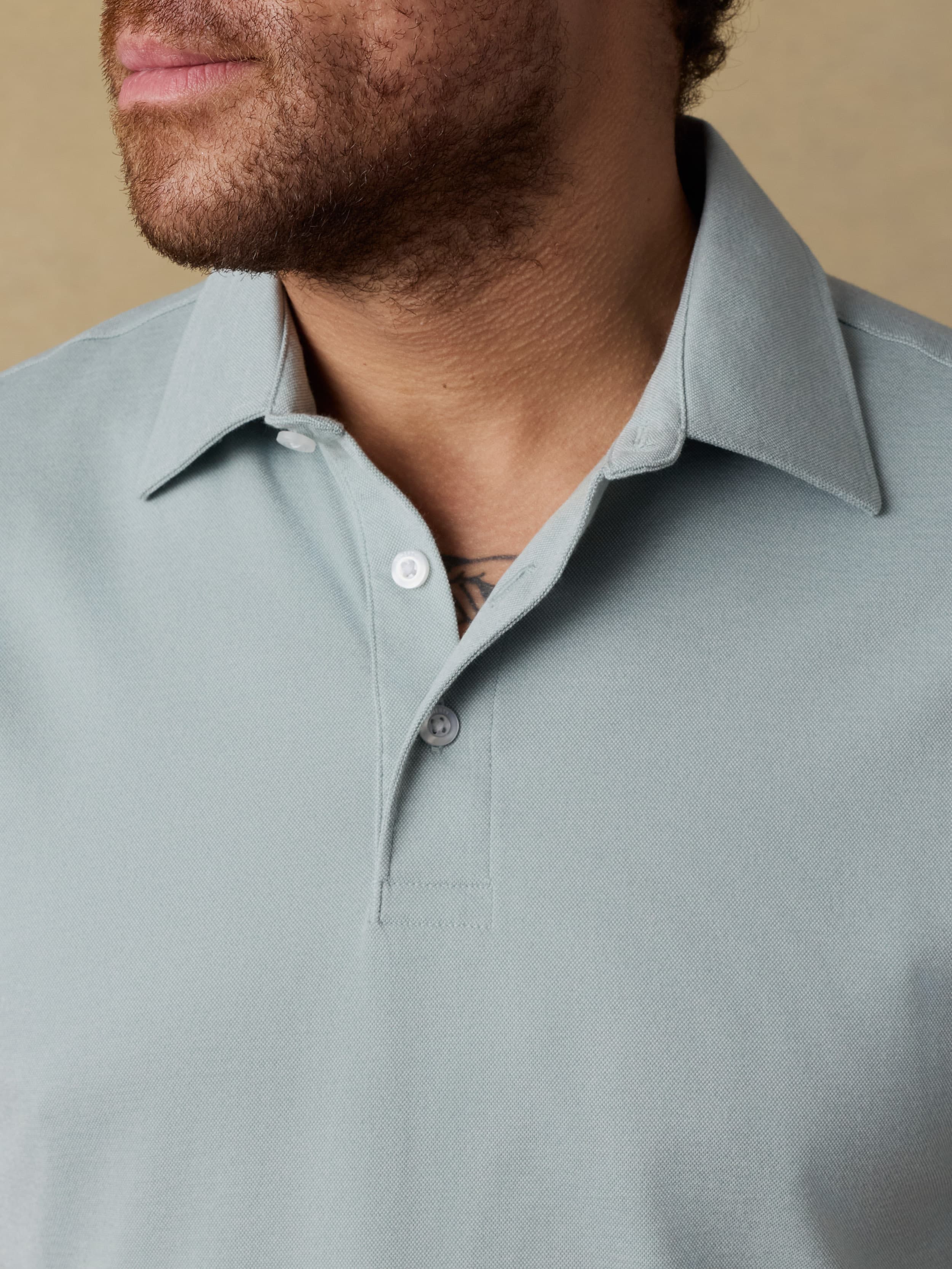 Close up shot of a man wearing a light green short sleeve polo shirt against a beige background