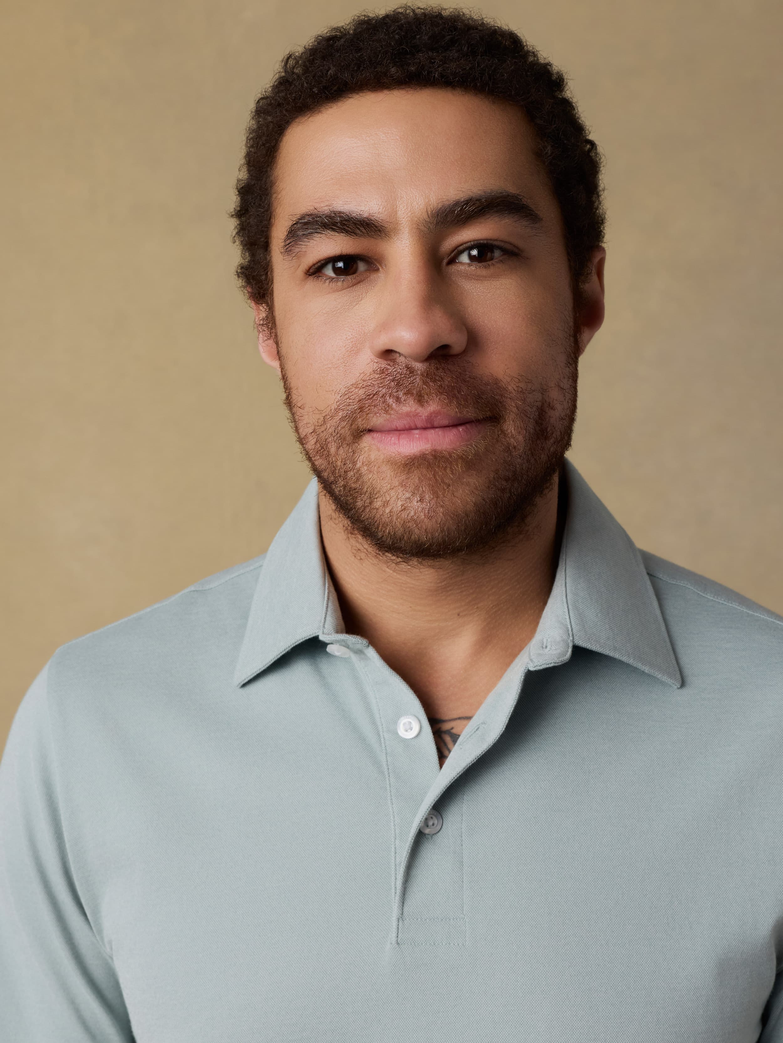 Close up shot of a man wearing a light green short sleeve polo shirt against a beige background