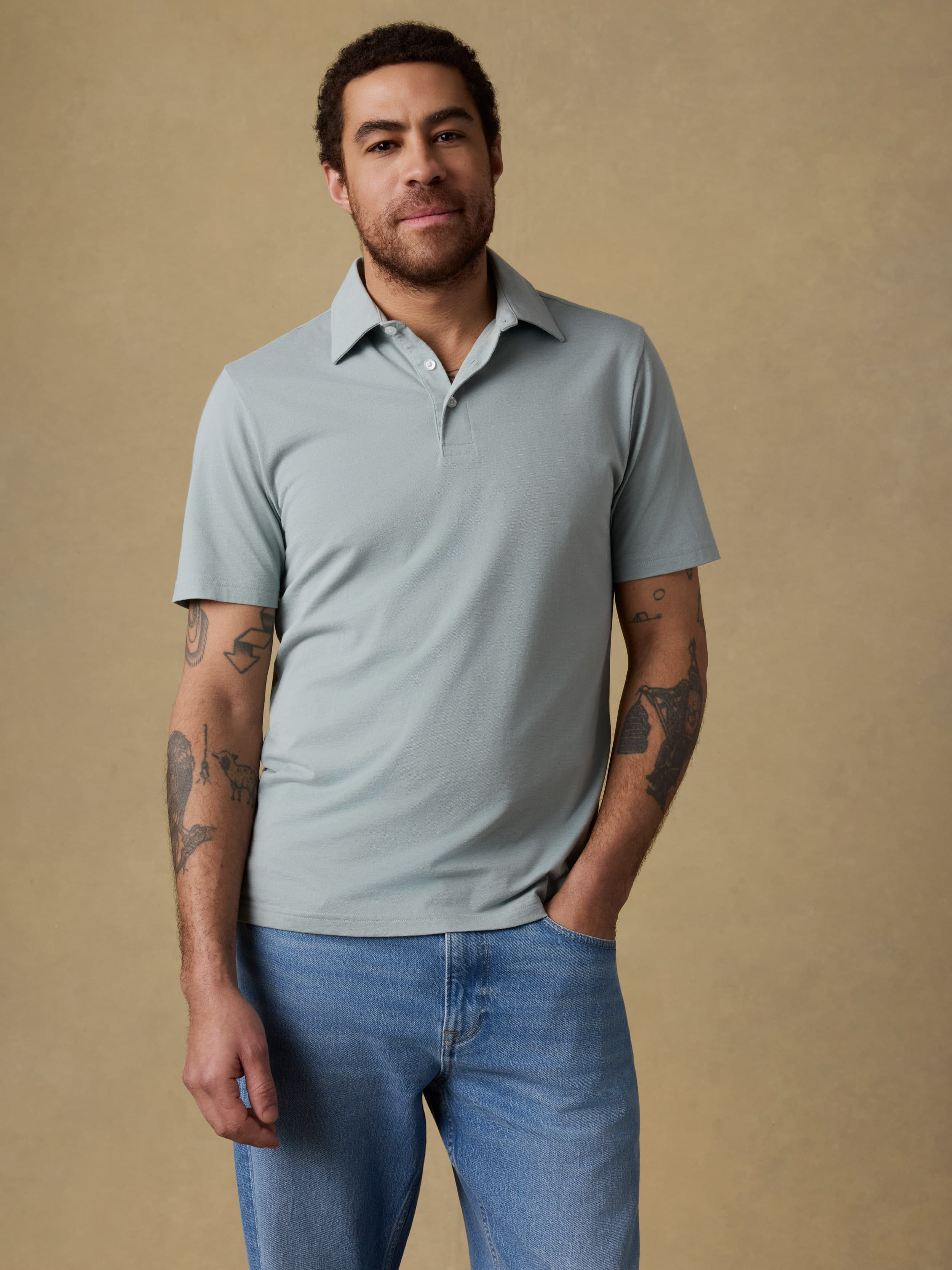 Man wearing a light green short sleeve polo shirt and blue jeans against a beige background