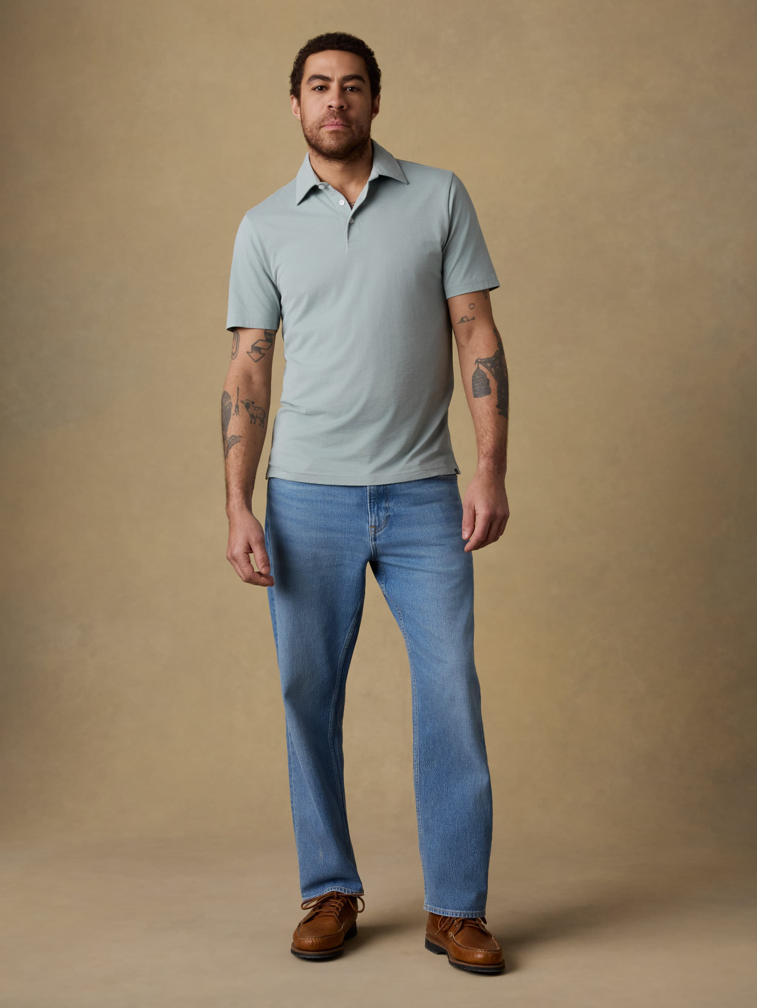 Man wearing a light green short sleeve polo shirt and blue jeans against a beige background