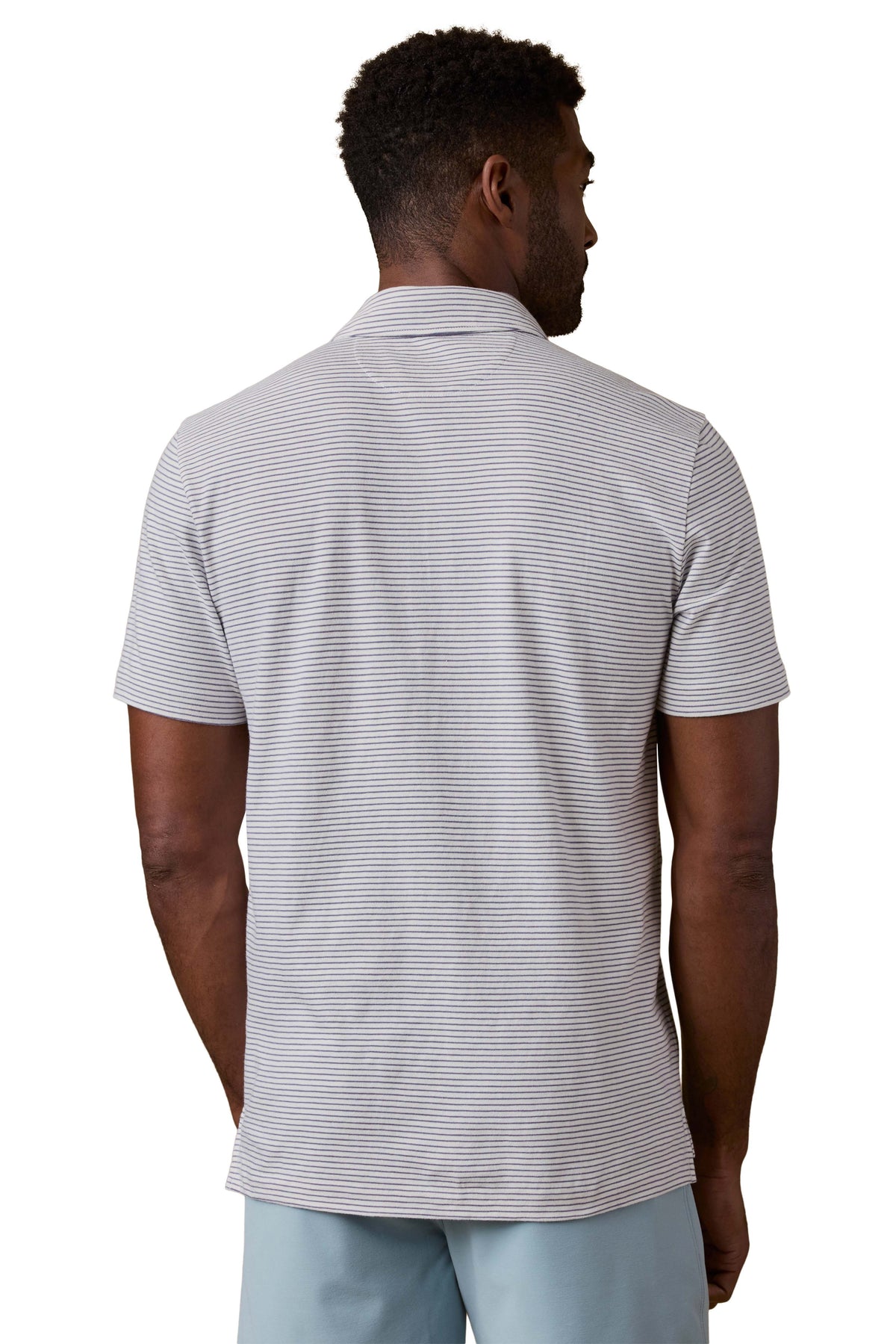A man viewed from behind wearing a striped polo shirt and blue shorts, image 3 of 3