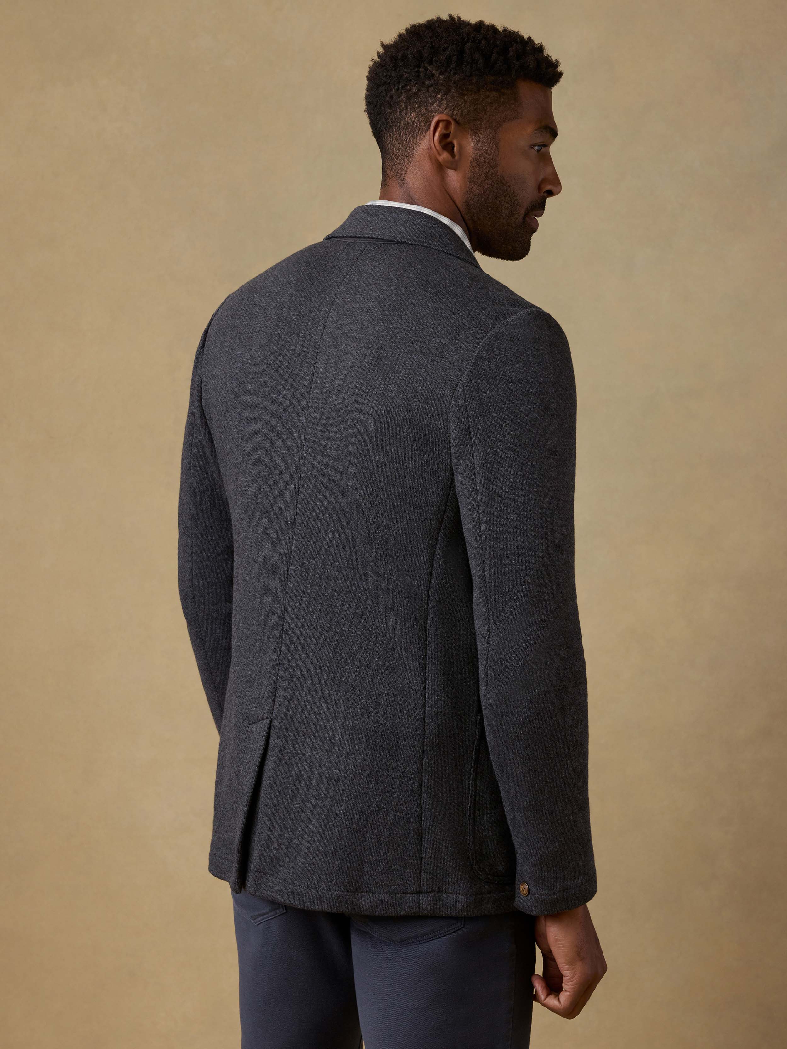 Back view of a man wearing a dark gray suit against a beige background