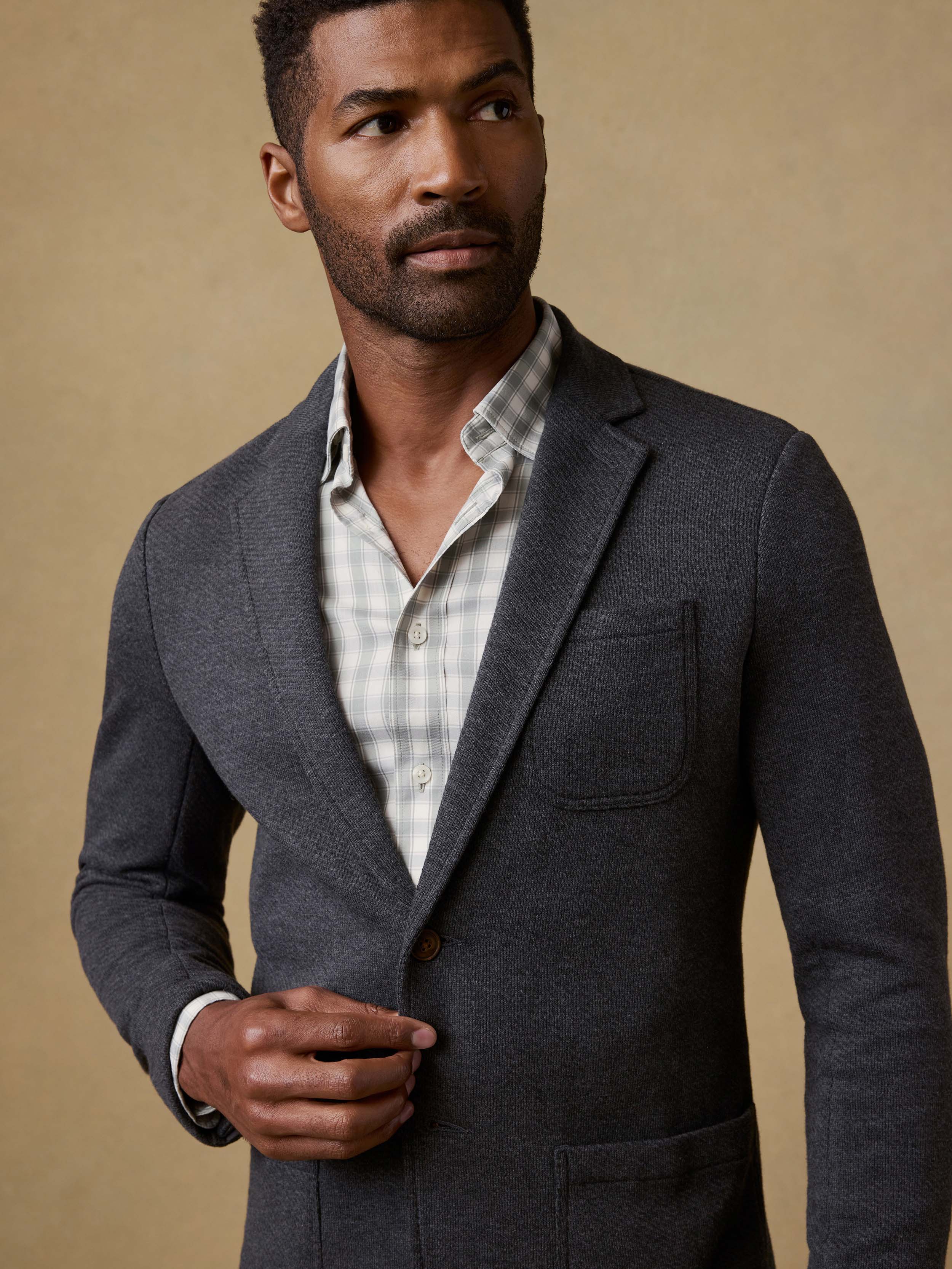 Man wearing a gray blazer over a plaid shirt against a beige background