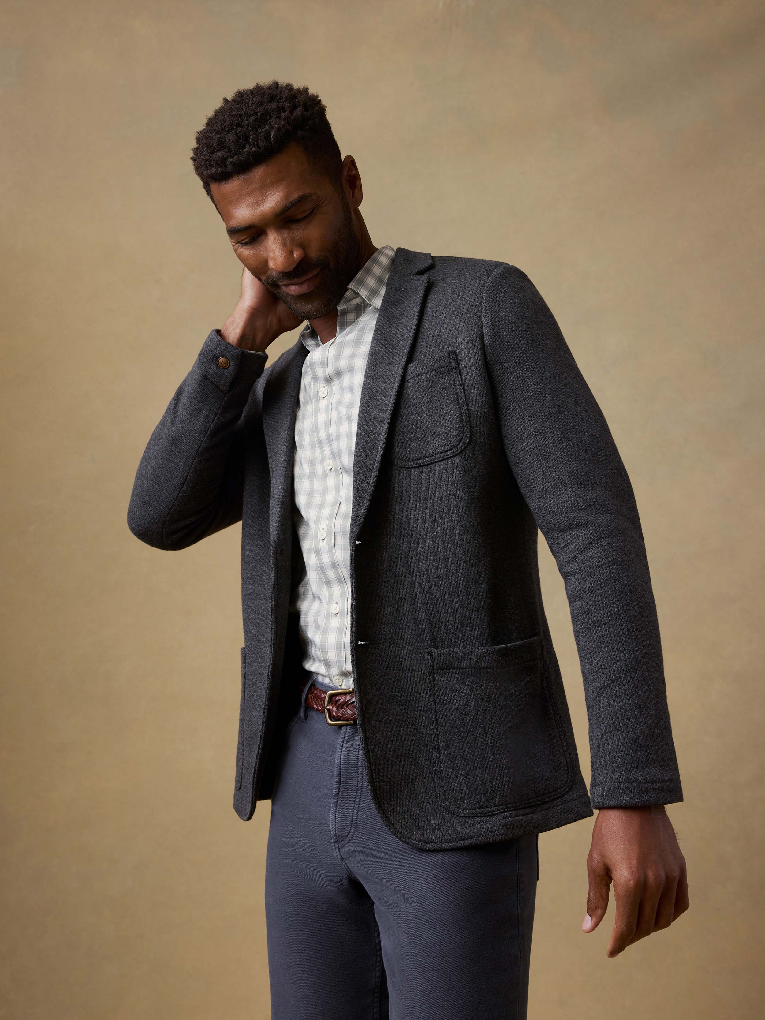 Man wearing a dark gray blazer over a checkered shirt with a beige background