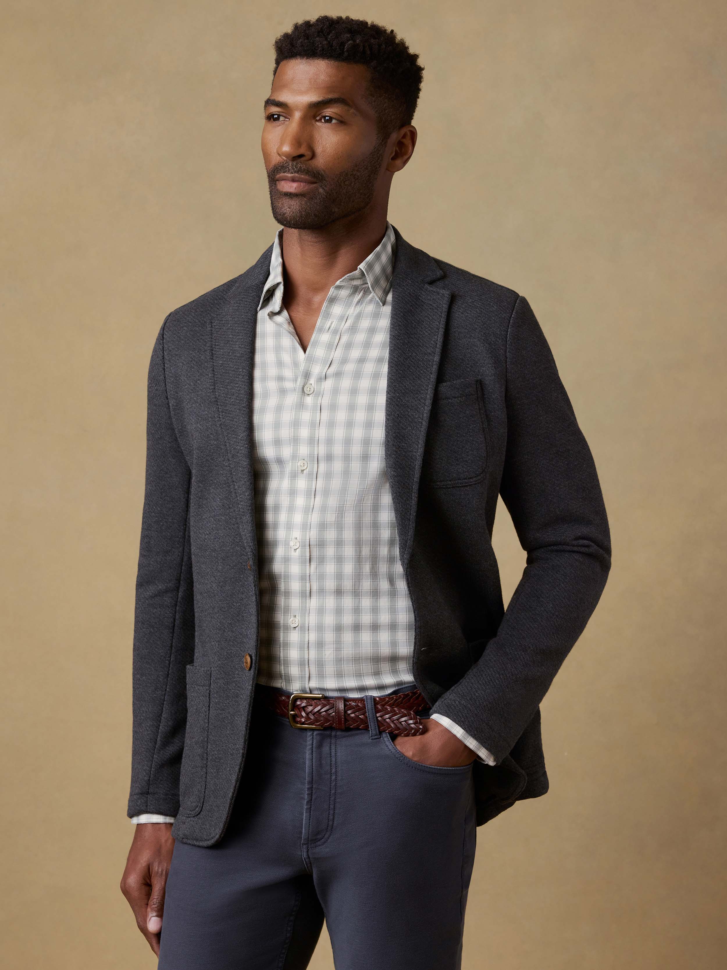 Man wearing a dark gray blazer over a plaid shirt with a beige background