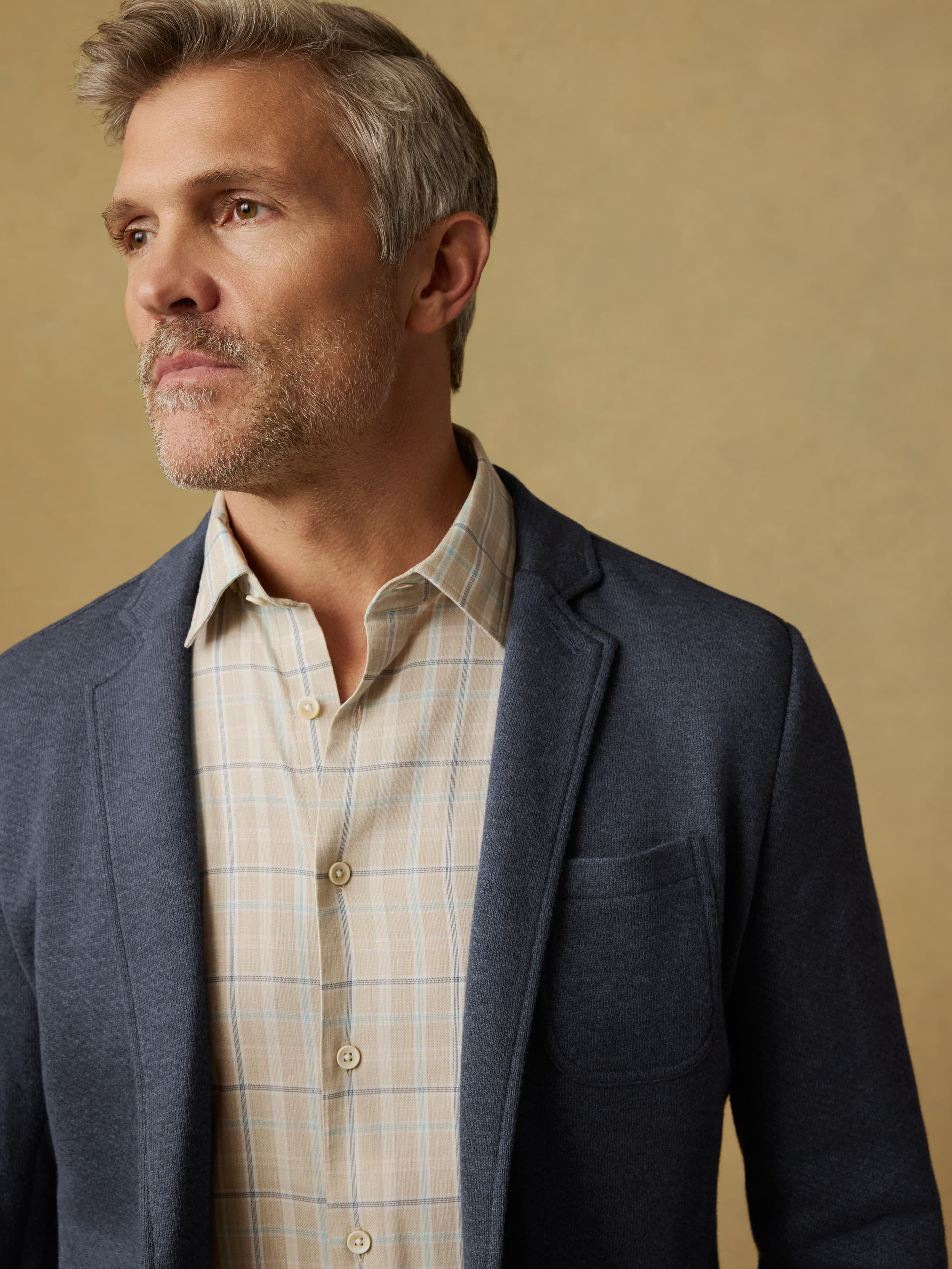 Man wearing a blue blazer over a plaid shirt against a beige background
