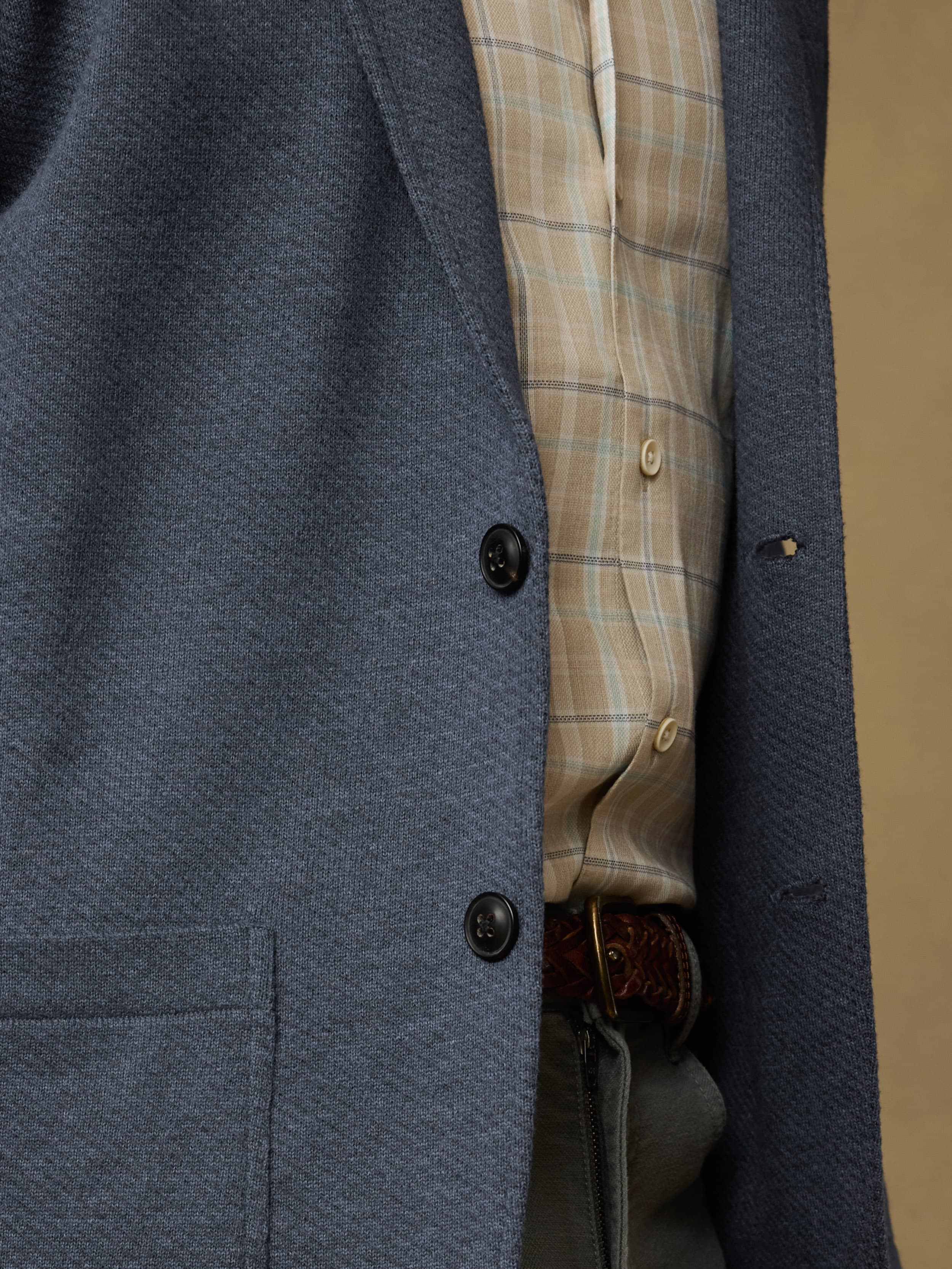 Close-up of a man  wearing a blue blazer over a plaid shirt with gray pants against a beige background