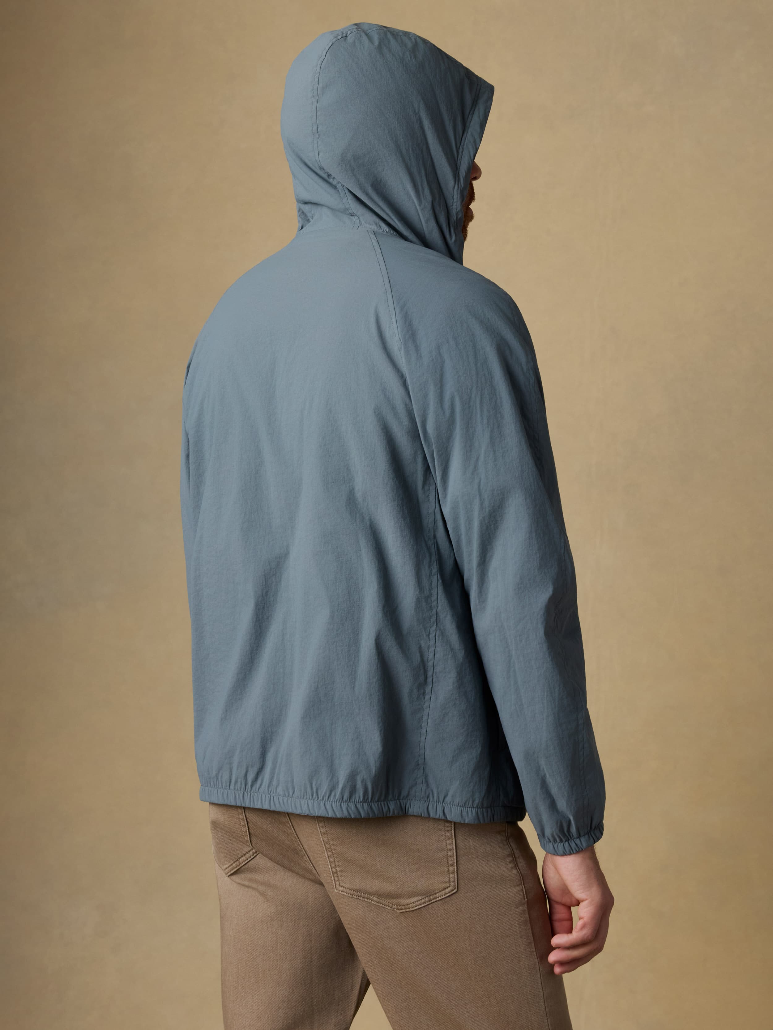 Back view of a man wearing a blue jacket and beige pants against a beige background