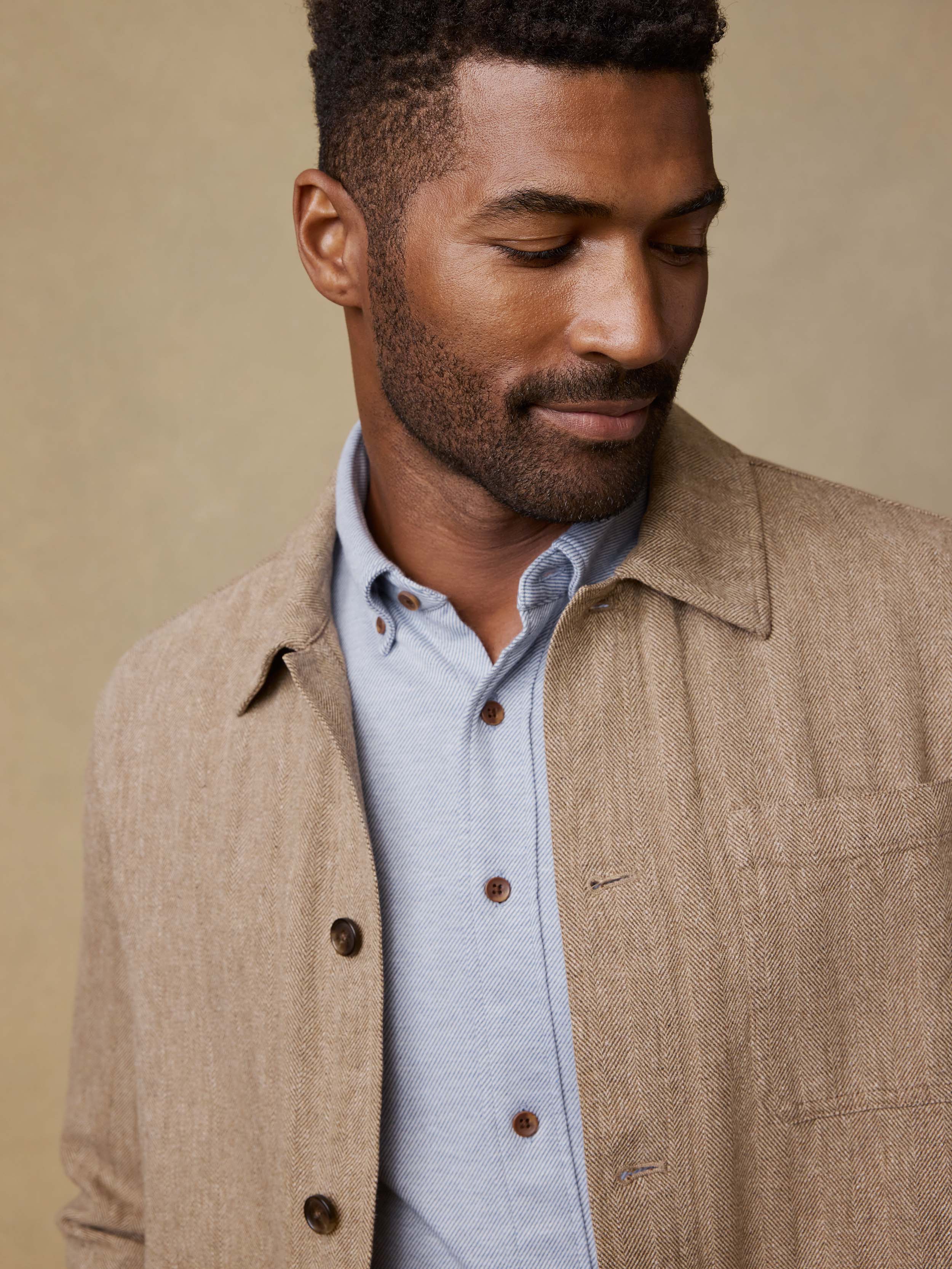 Man wearing a beige jacket over a light blue shirt against a beige background