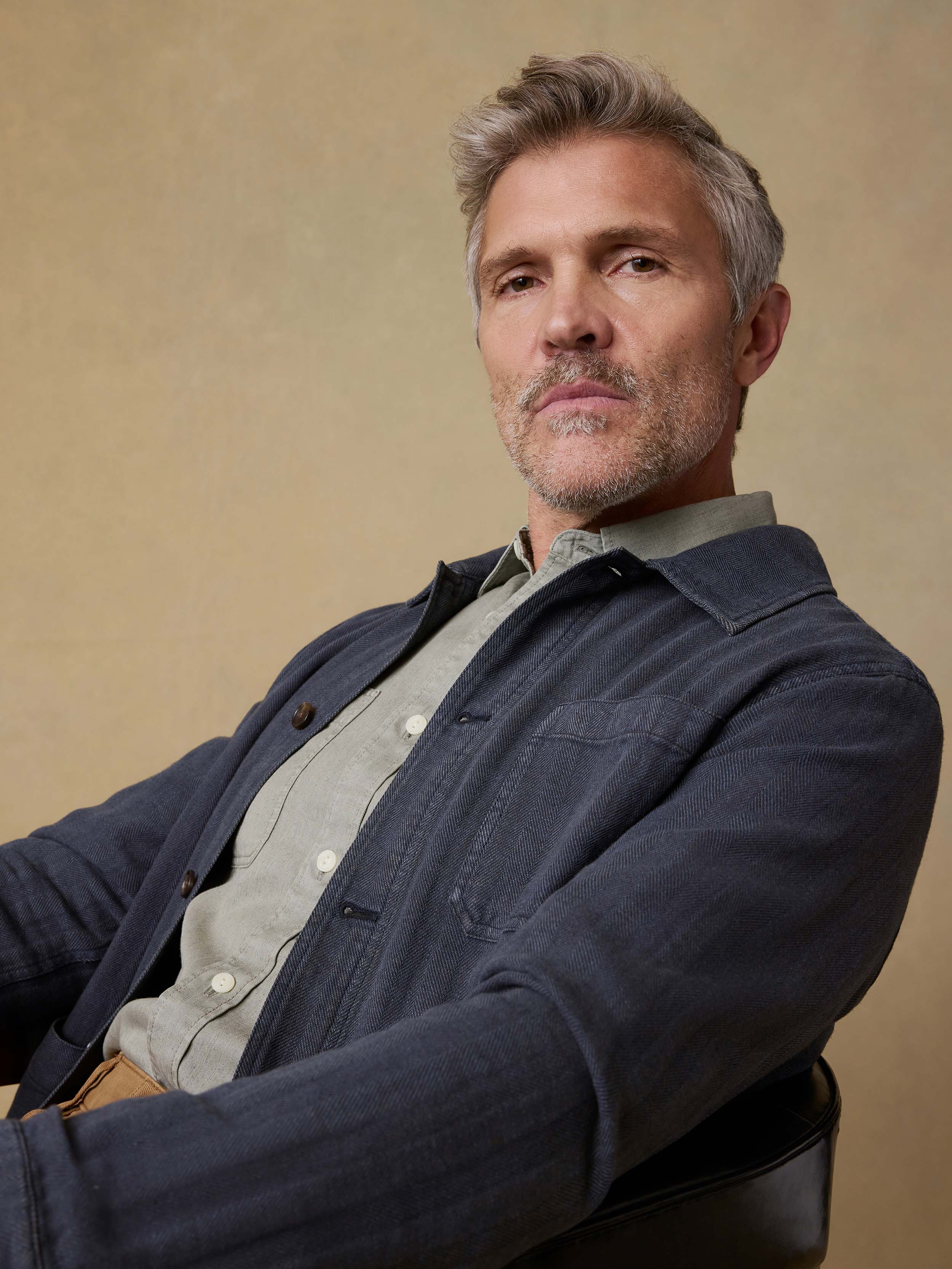 Man wearing a dark jacket over a light green shirt against a beige background