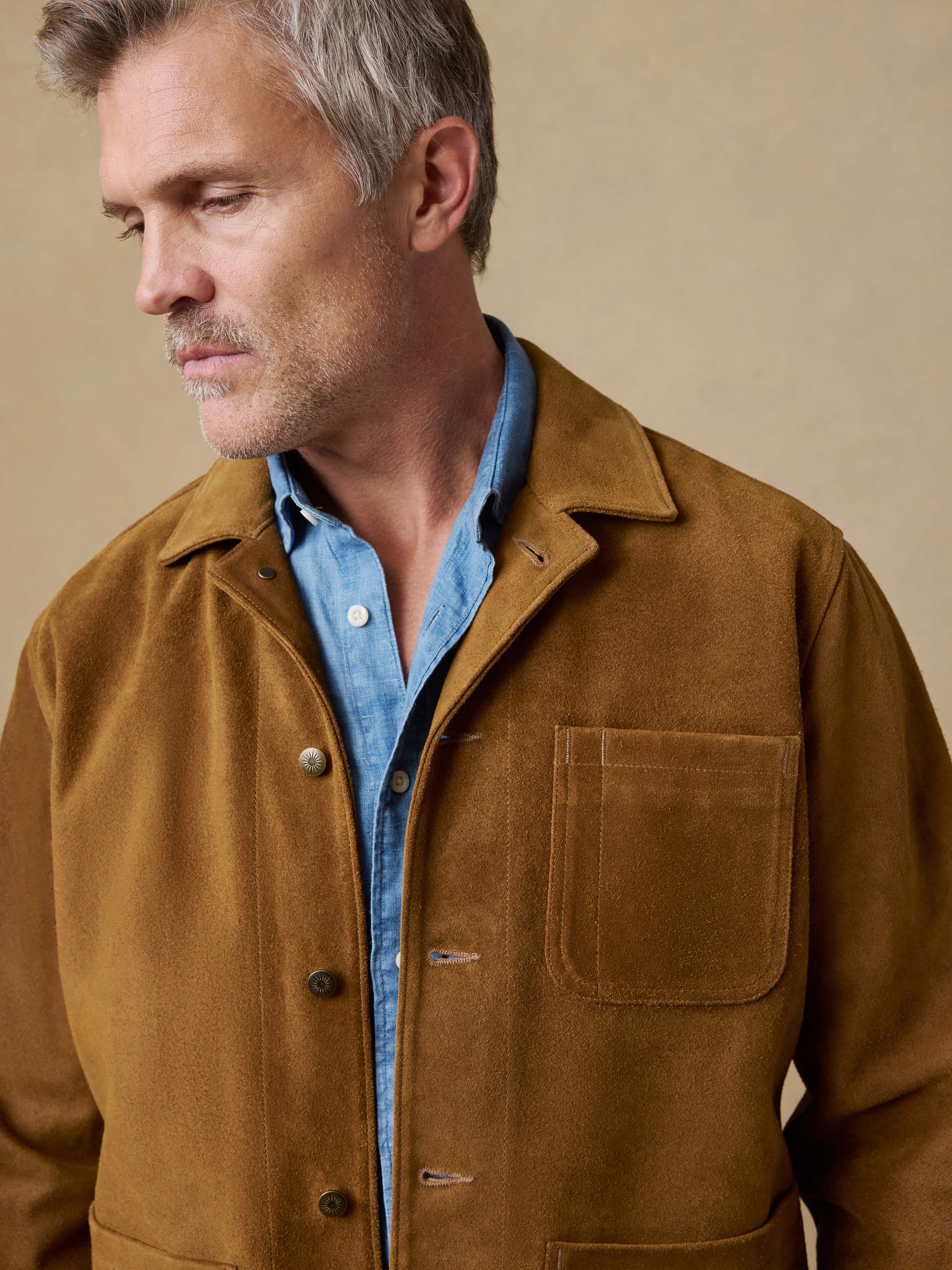 Man wearing a brown suede  jacket over a blue shirt on a beige background