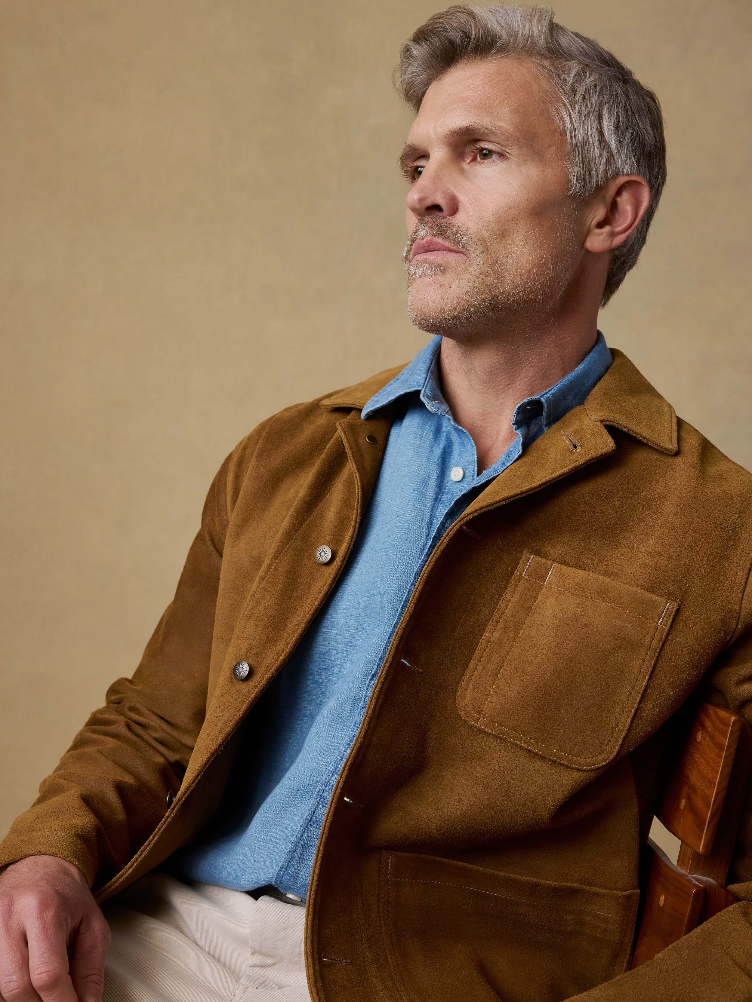 Man wearing a brown suede  jacket over a blue shirt on a beige background
