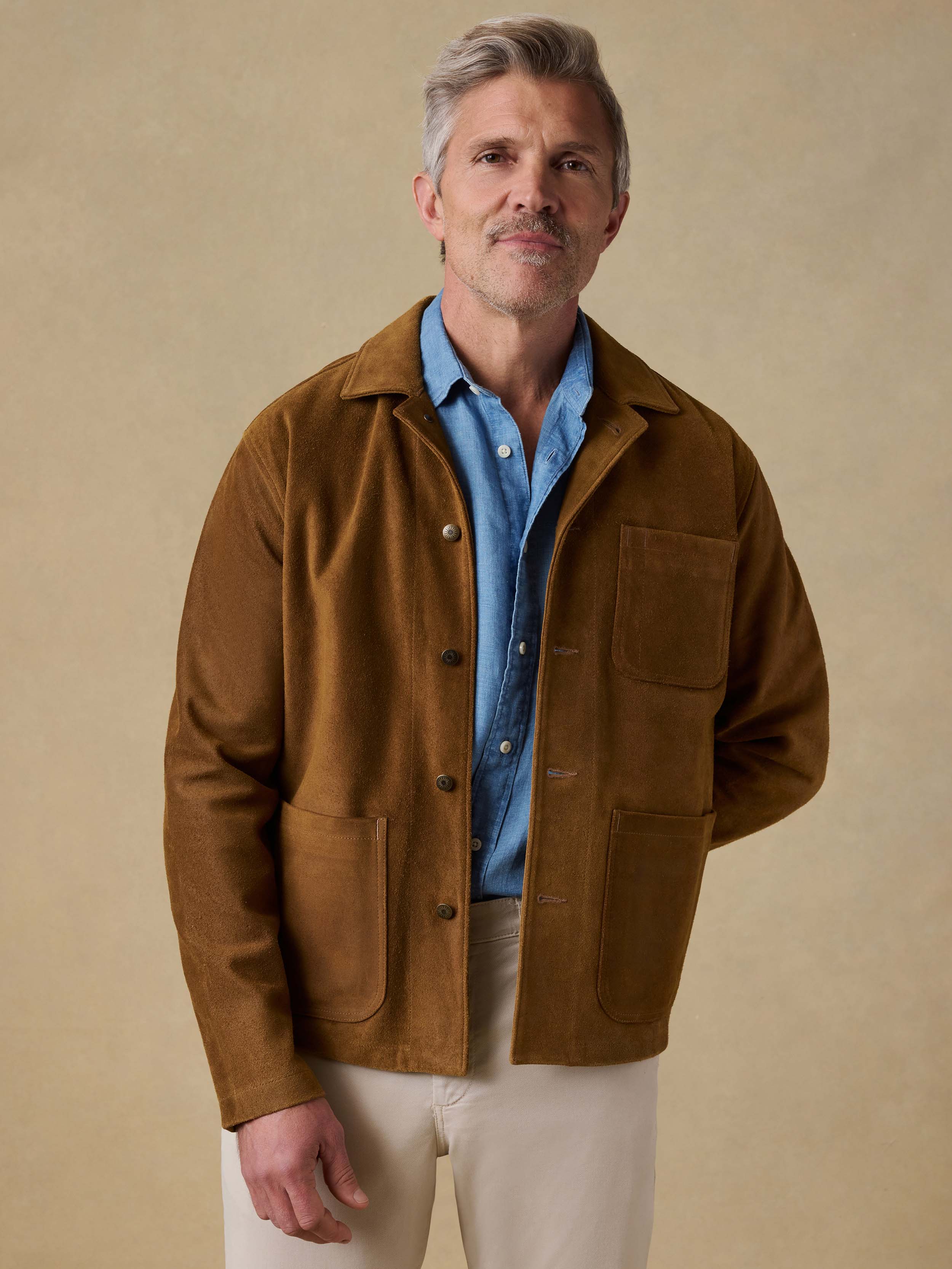 Man wearing a brown suede  jacket over a blue shirt on a beige background
