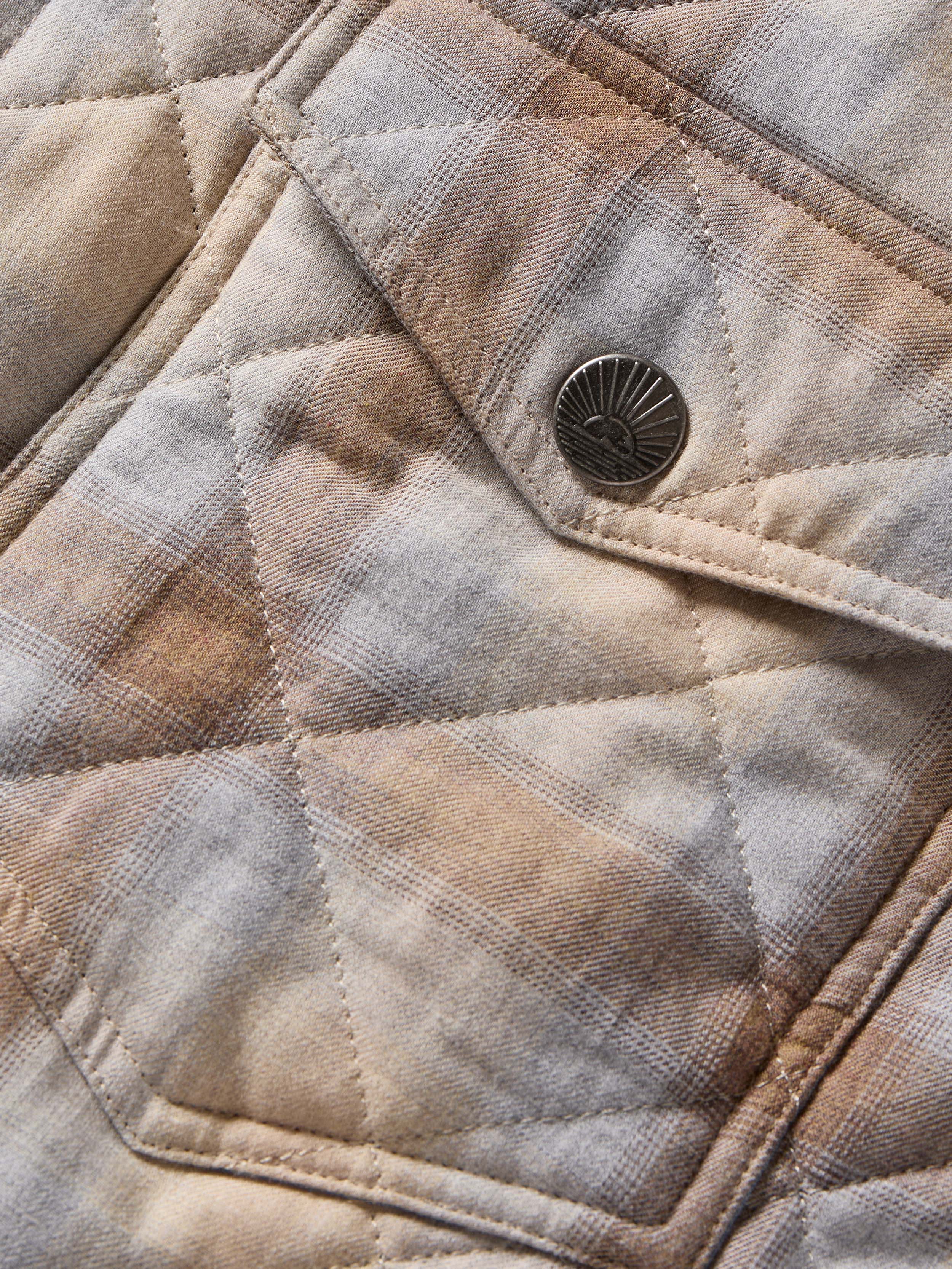 Close-up of a quilted jacket with a button, showing texture and pattern details.