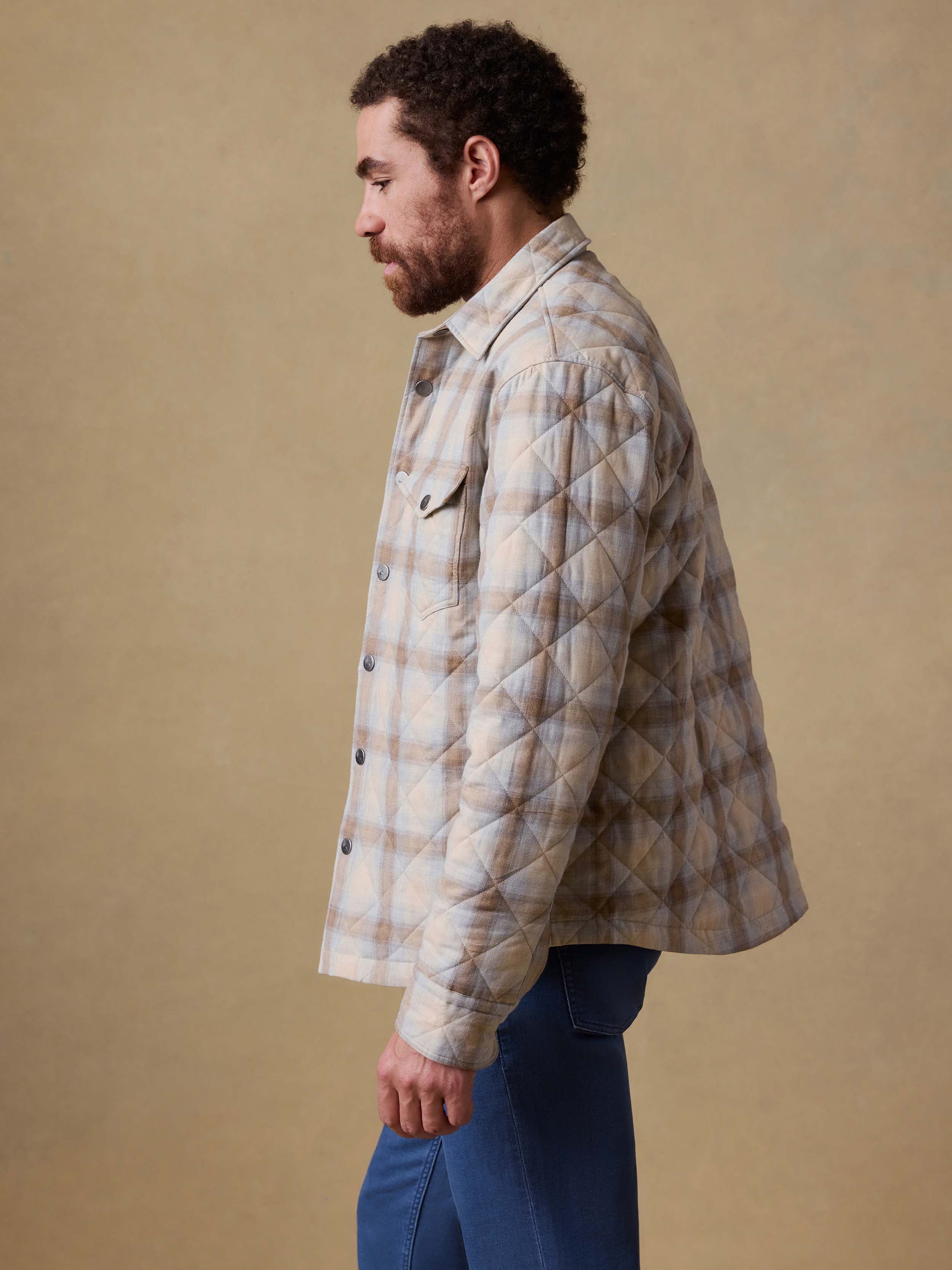 Man wearing a quilted plaid shirt jacket and blue jeans against a beige background