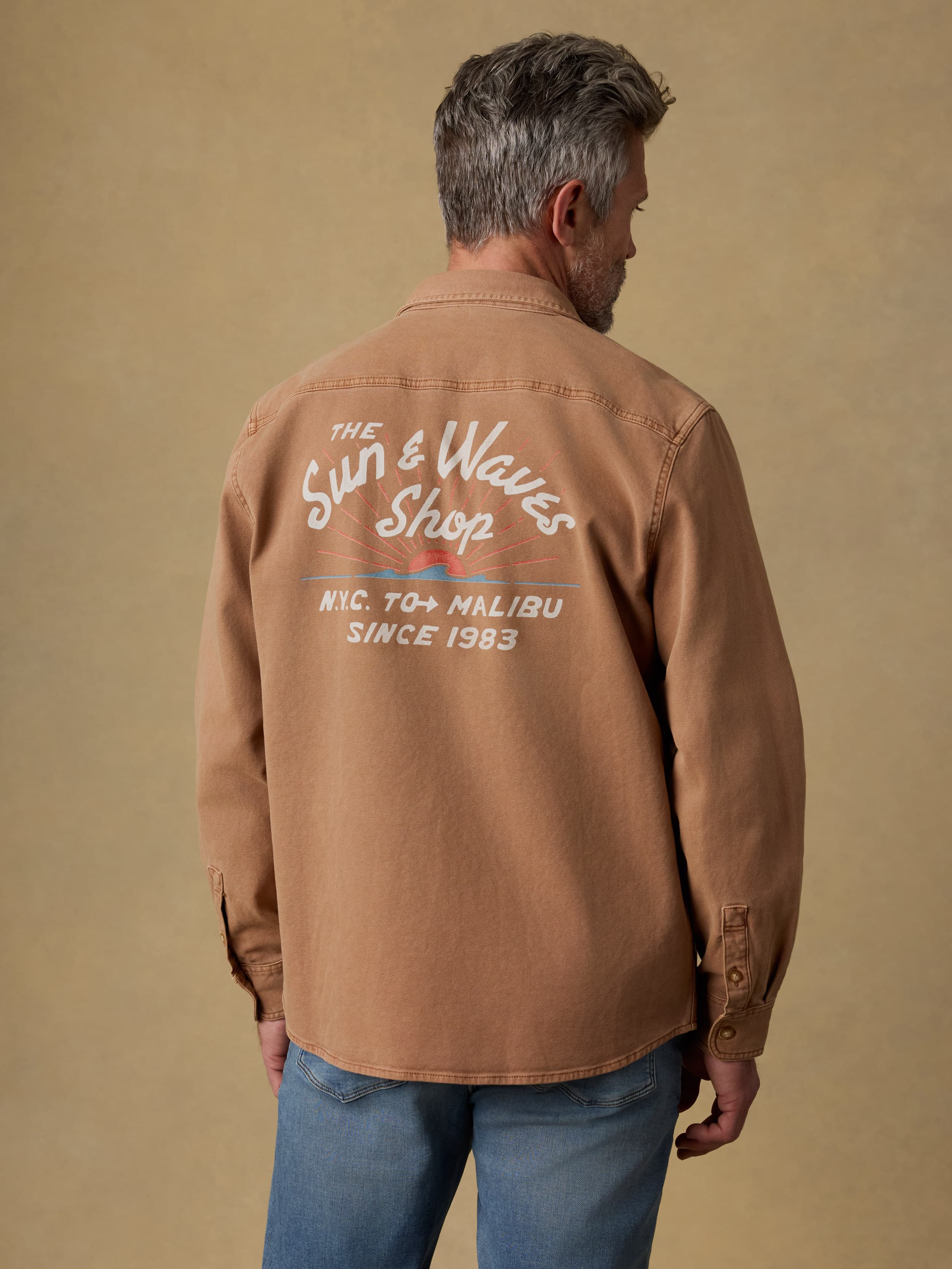 Back view of a man wearing a brown jacket with a Faherty graphic on the back against a beige background