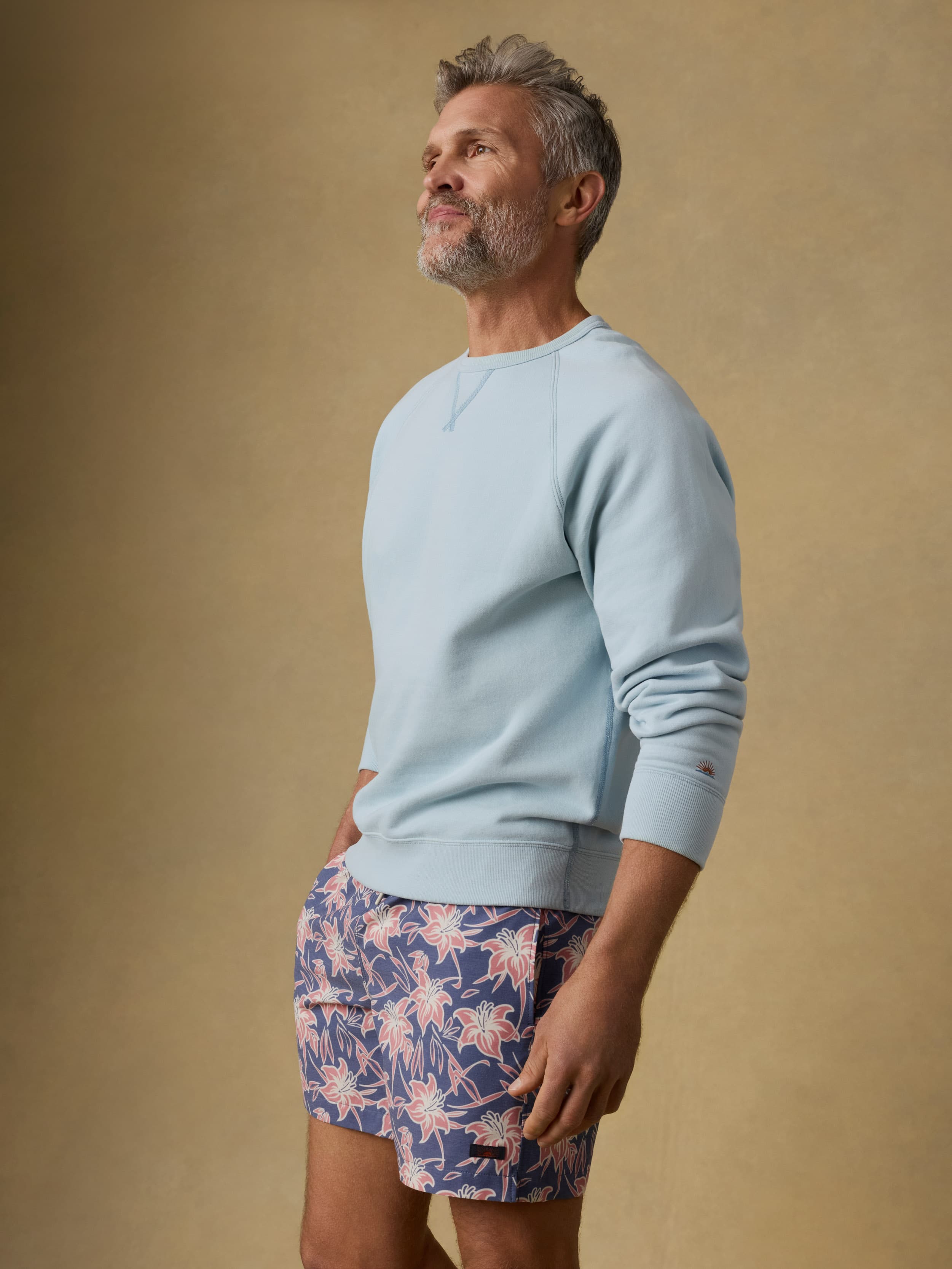 Man wearing a light blue crewneck sweatshirt and floral shorts against a beige background