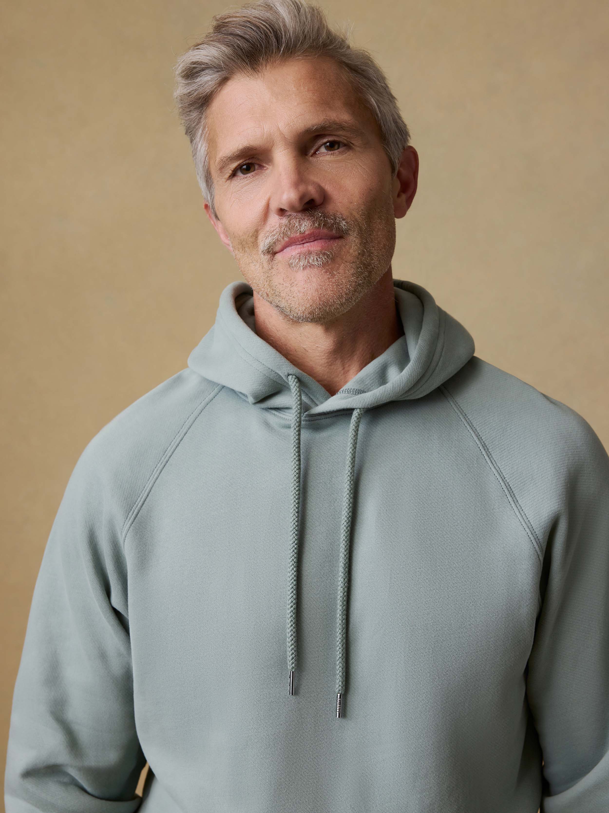 Man wearing a light green hoodie against a beige background