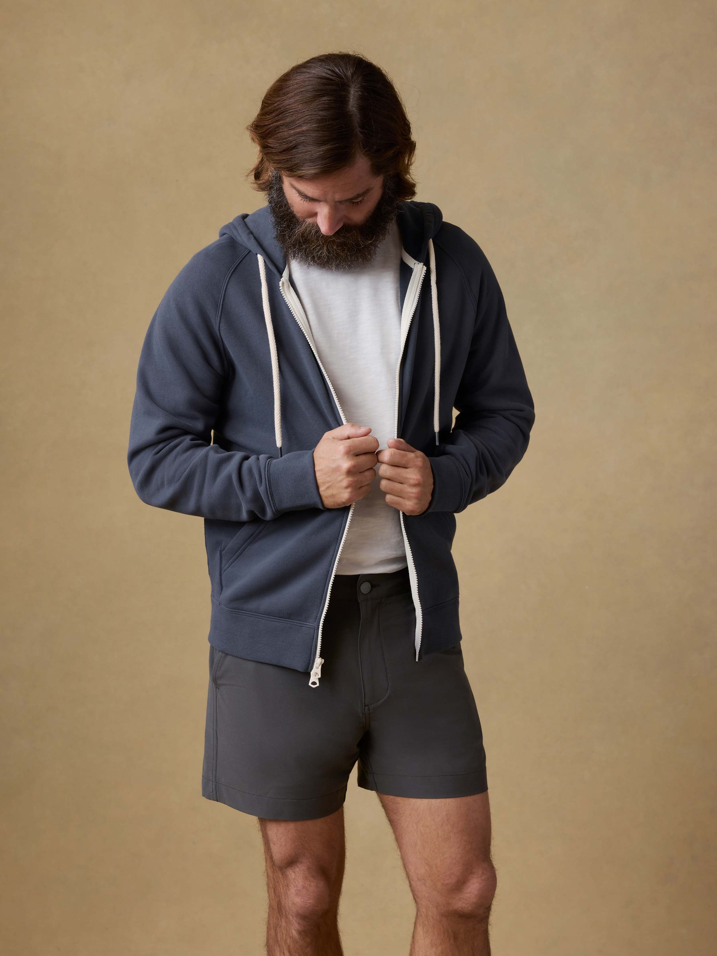 Man wearing a navy blue hoodie and gray shorts against a beige background