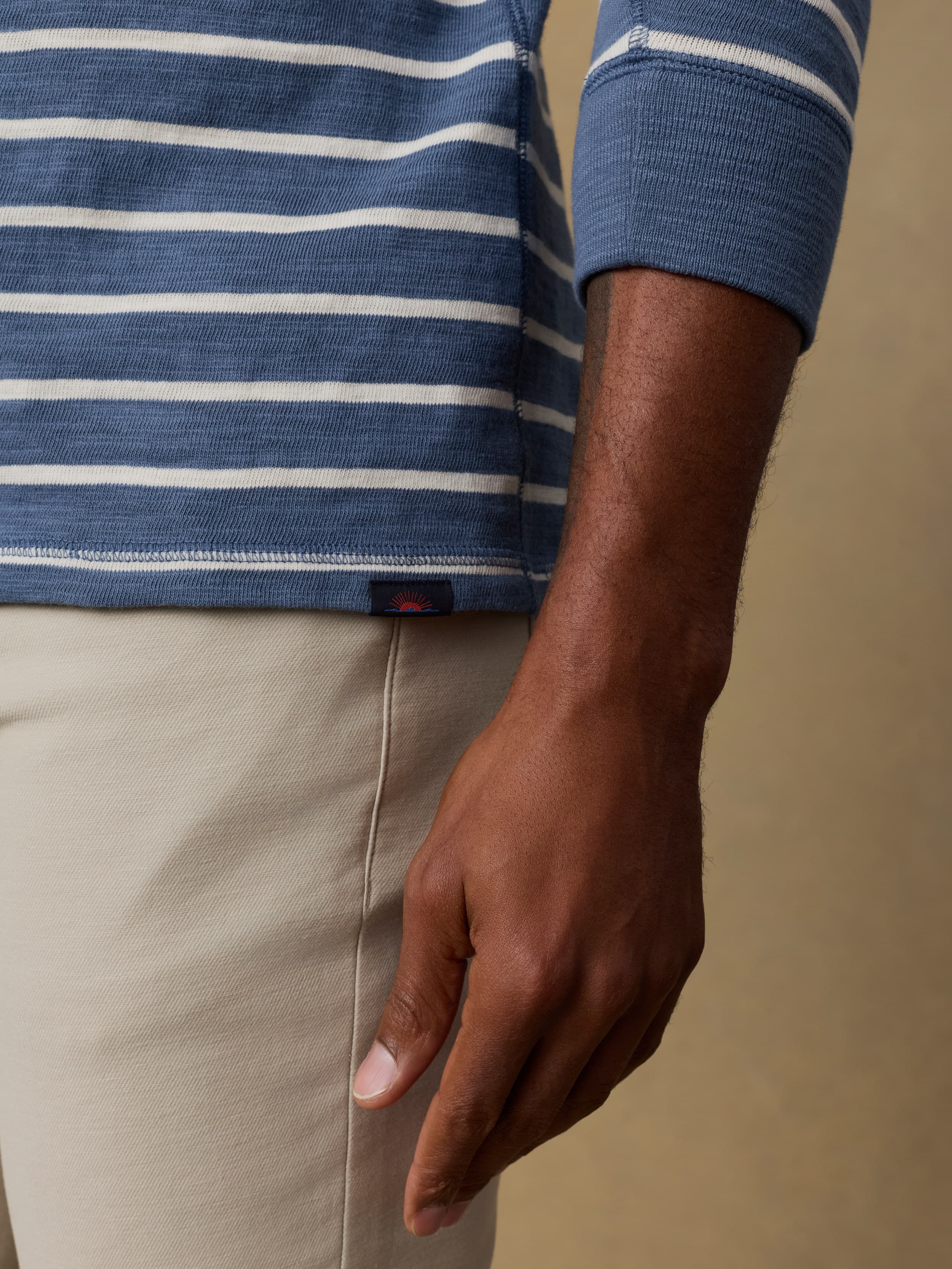 Close up shot of a man wearing a blue and white striped çrewneck sweatshirt with beige pants on a beige background