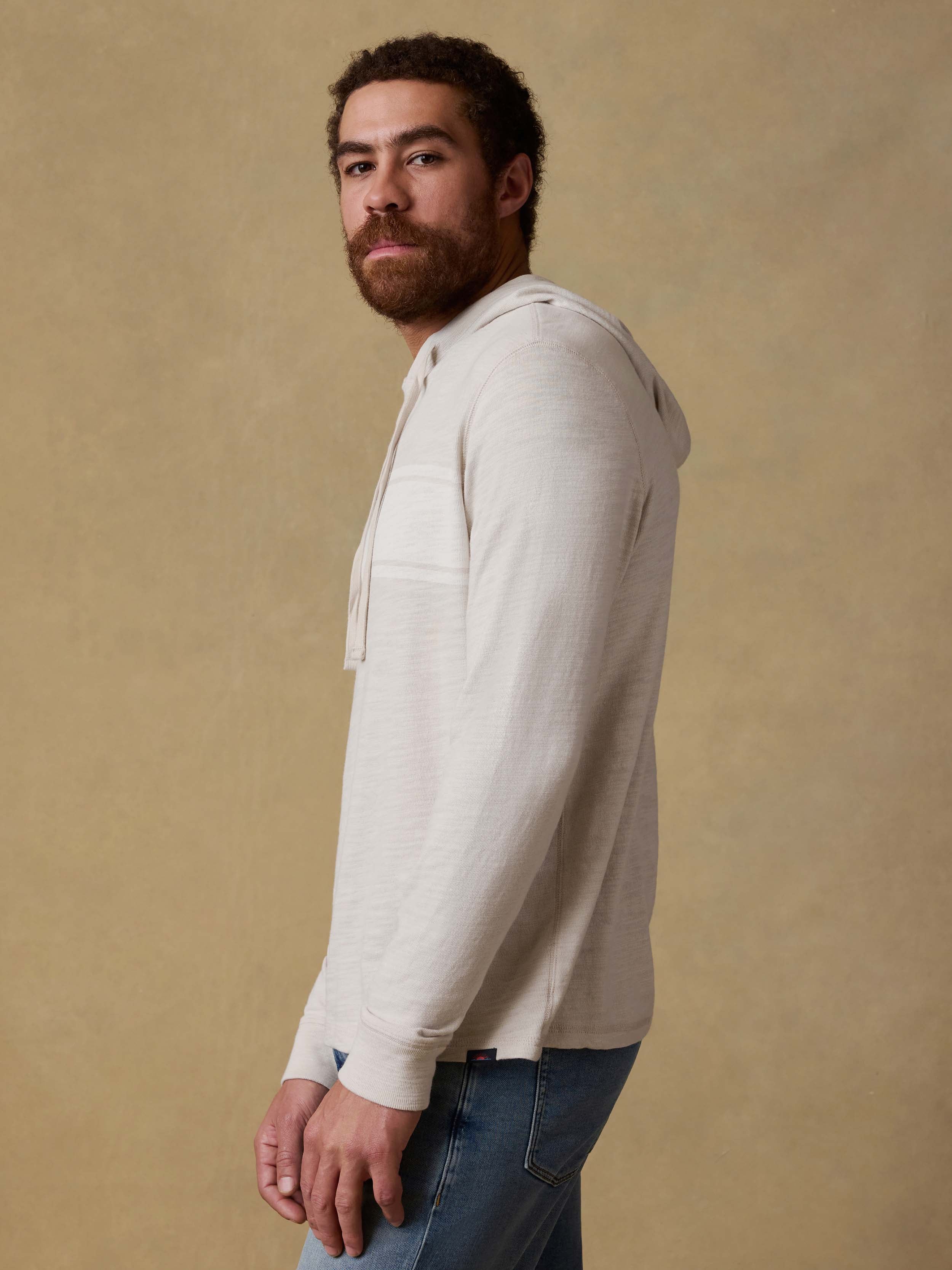 Man wearing a beige hoodie and blue jeans against a beige background