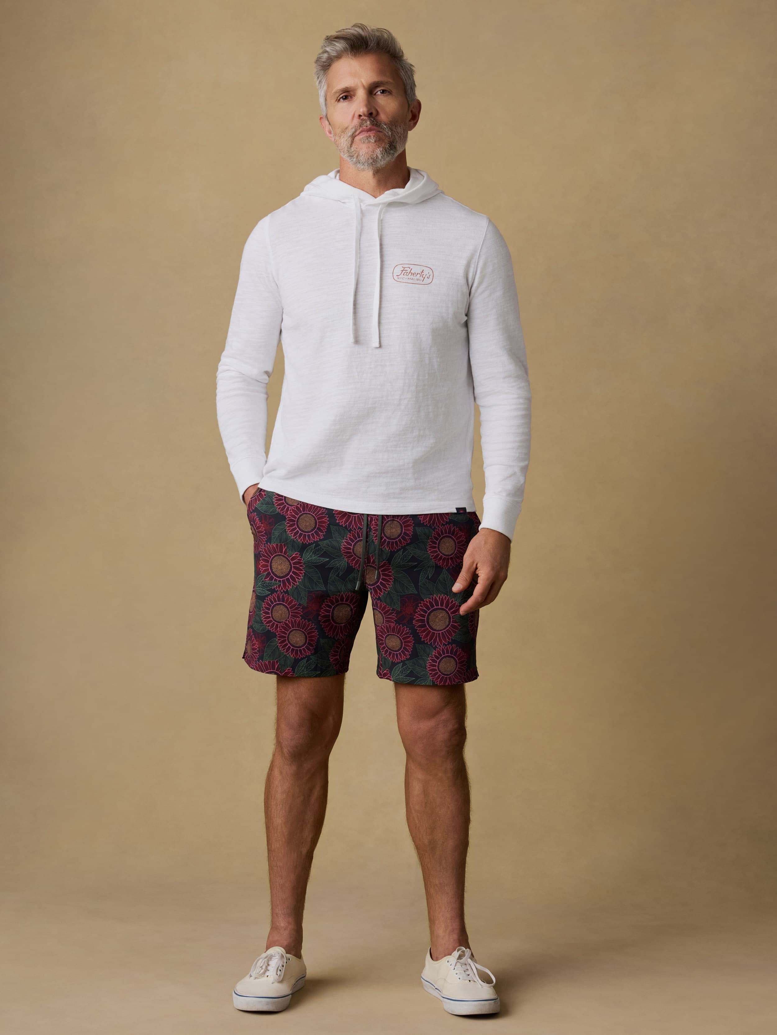 Man wearing a white hoodie with Faherty brand logo at the left chest and patterned shorts on a beige background