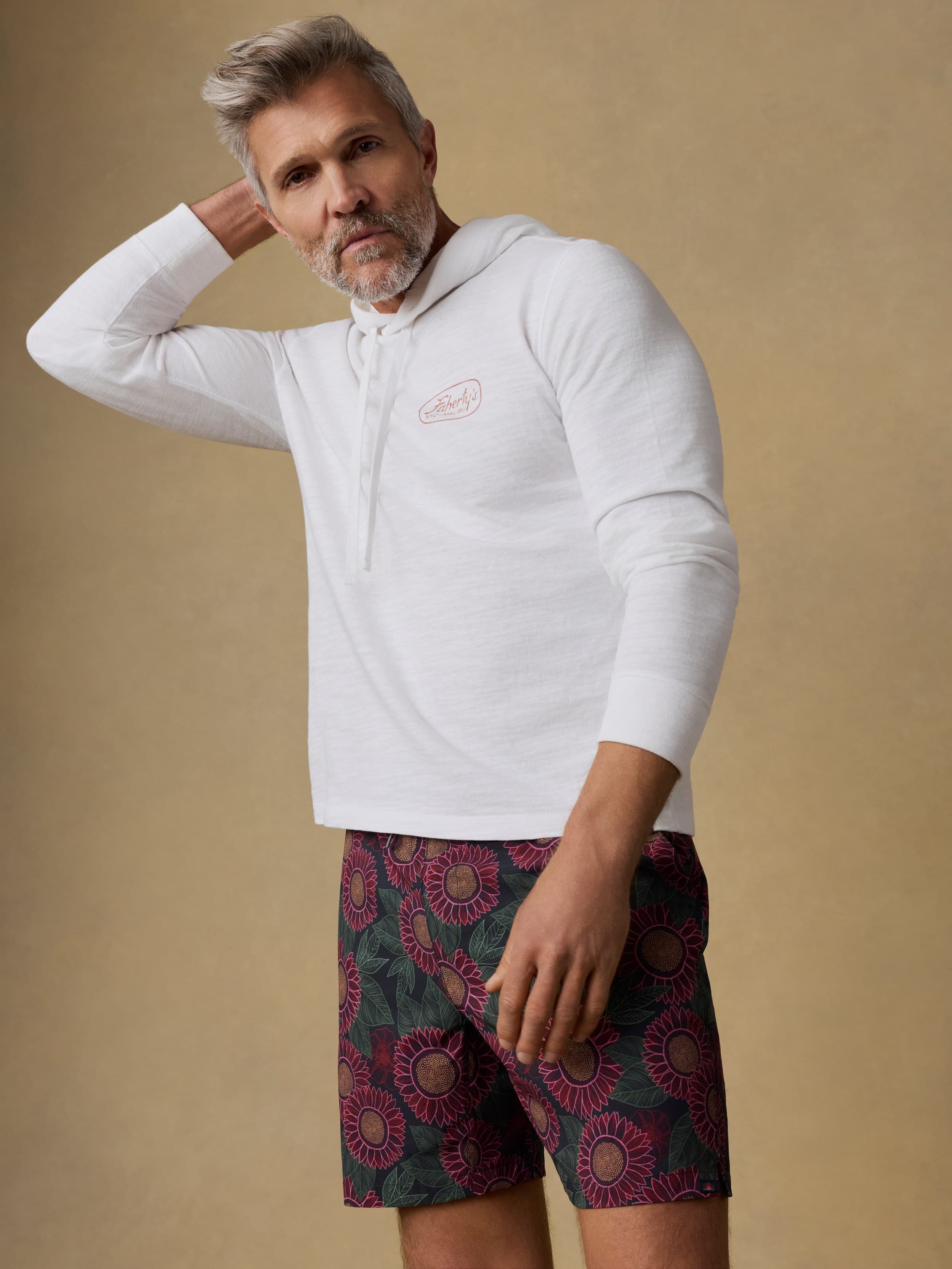 Man wearing a white hoodie and patterned swim trunks against a beige background