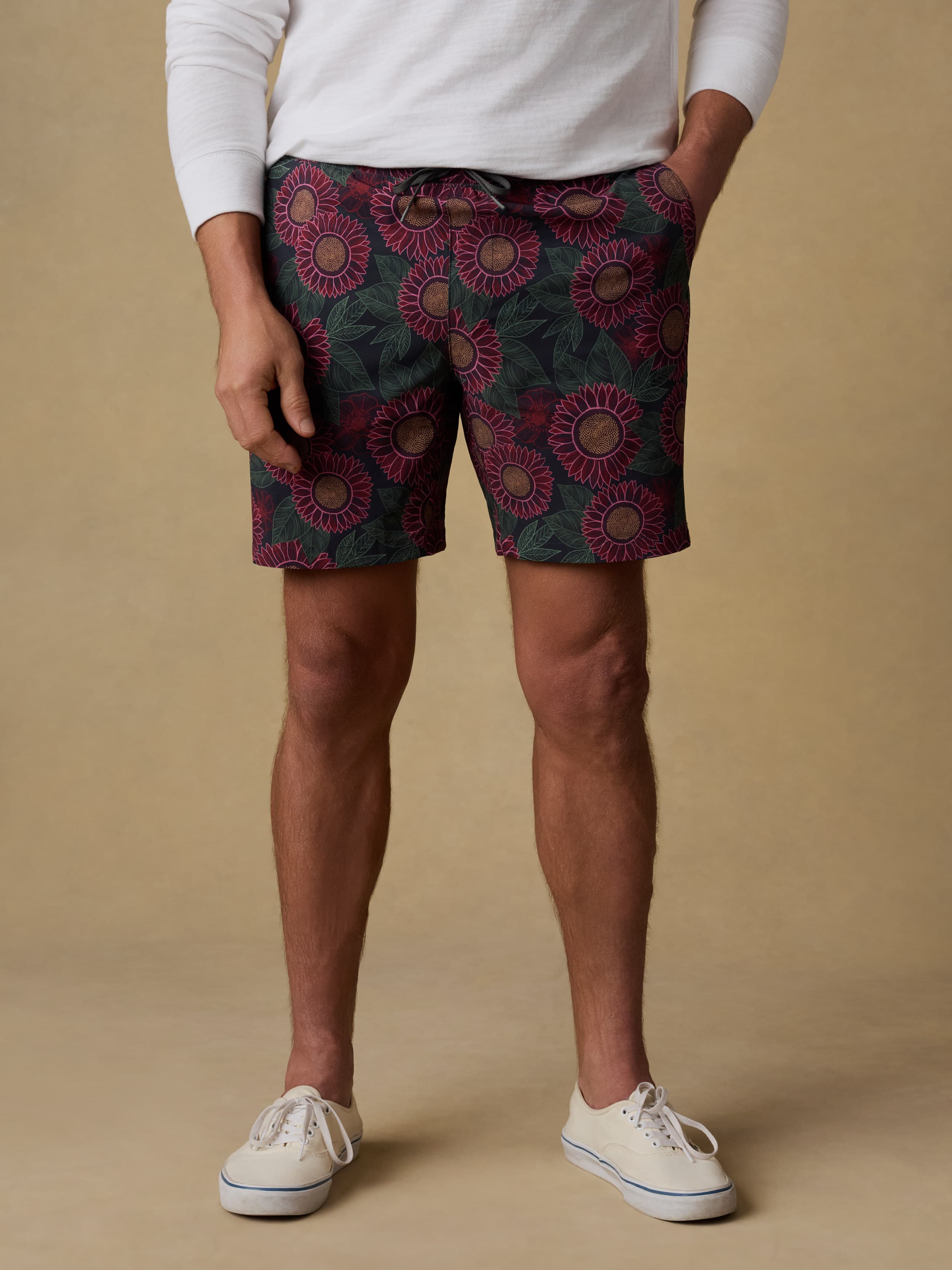 Man wearing a white hoodie and patterned swim trunks against a beige background