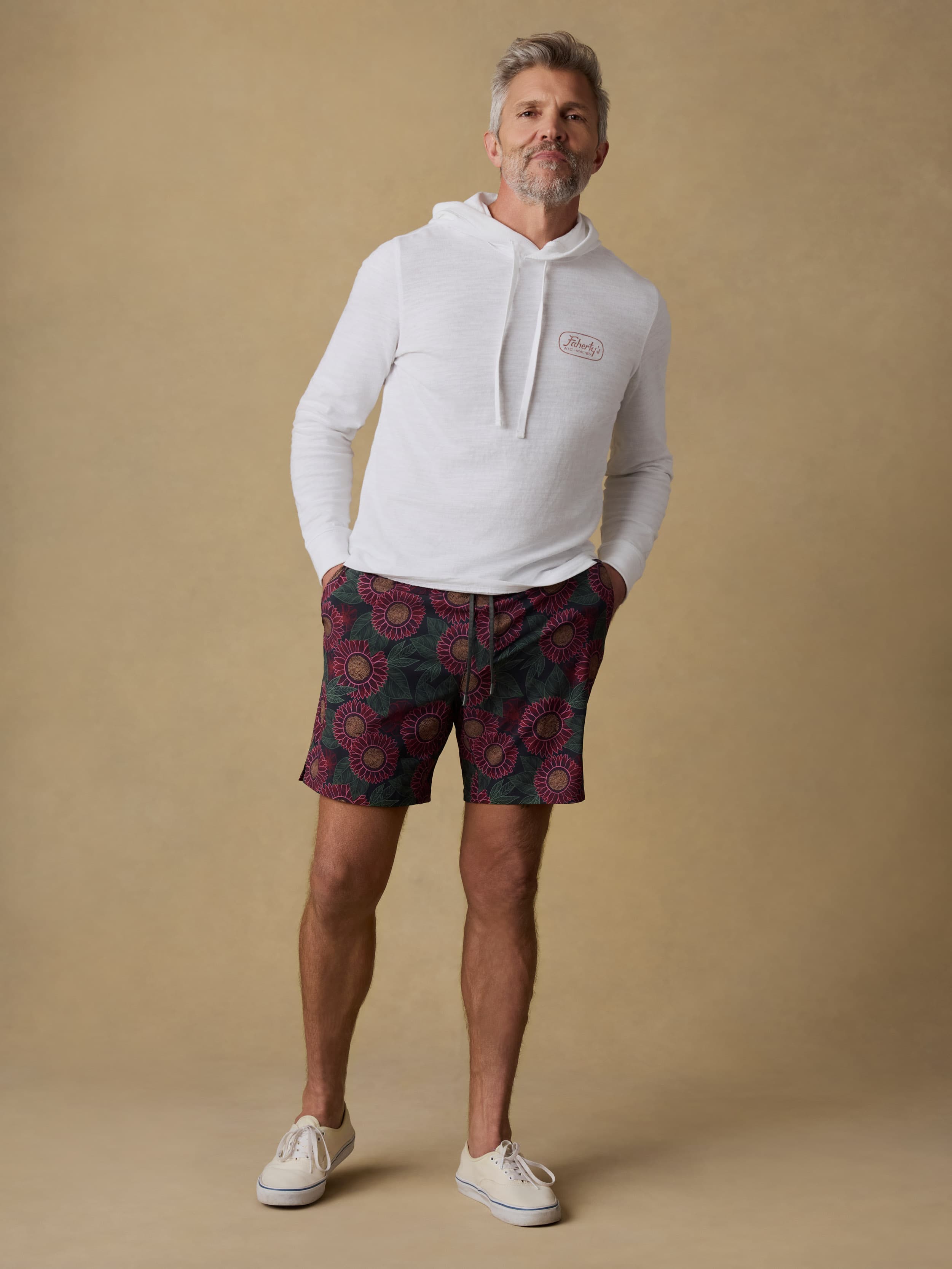 Man wearing a white hoodie and patterned swim trunks against a beige background