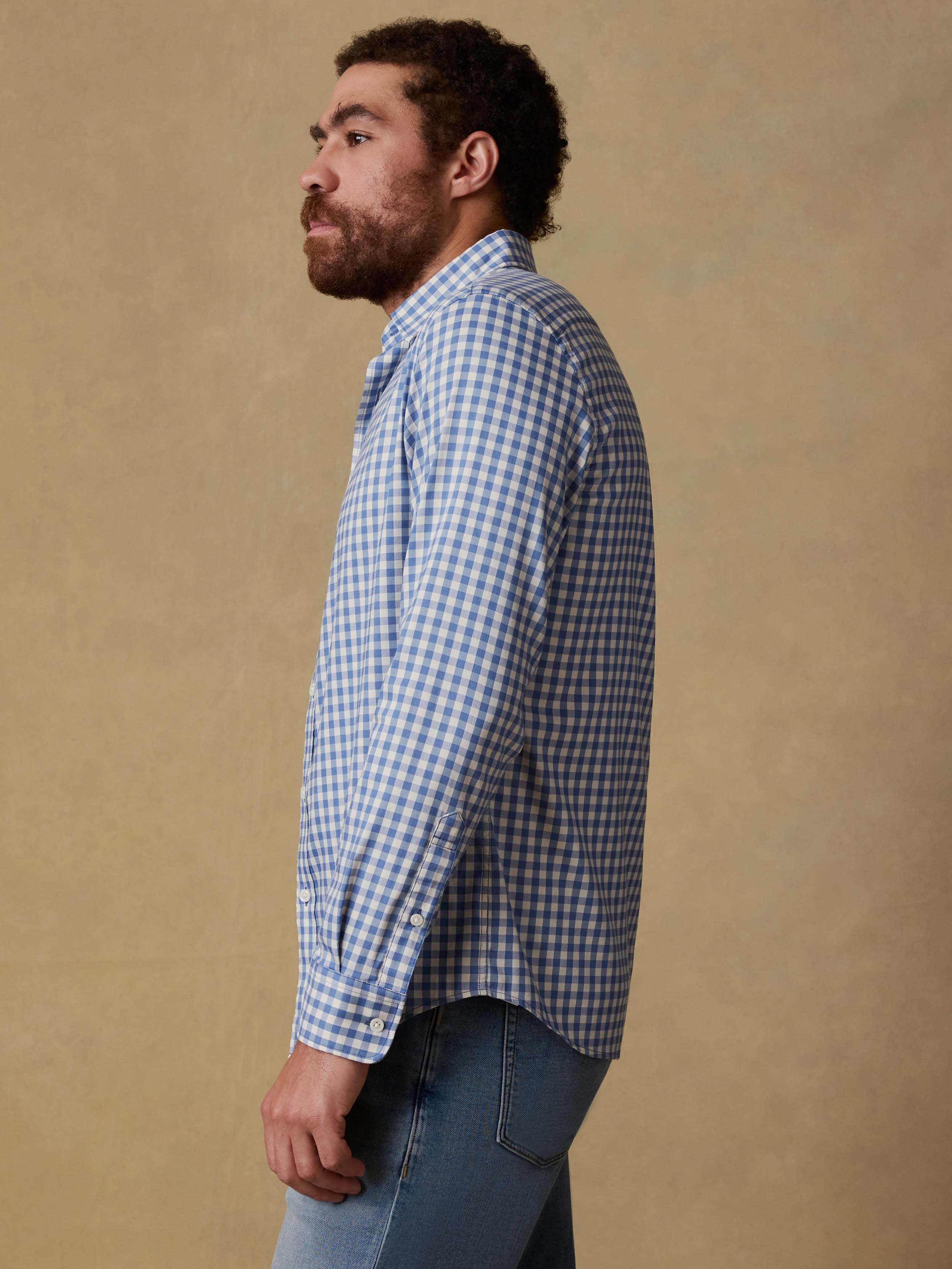 Man wearing a blue and white checkered shirt and blue jeans against a beige background