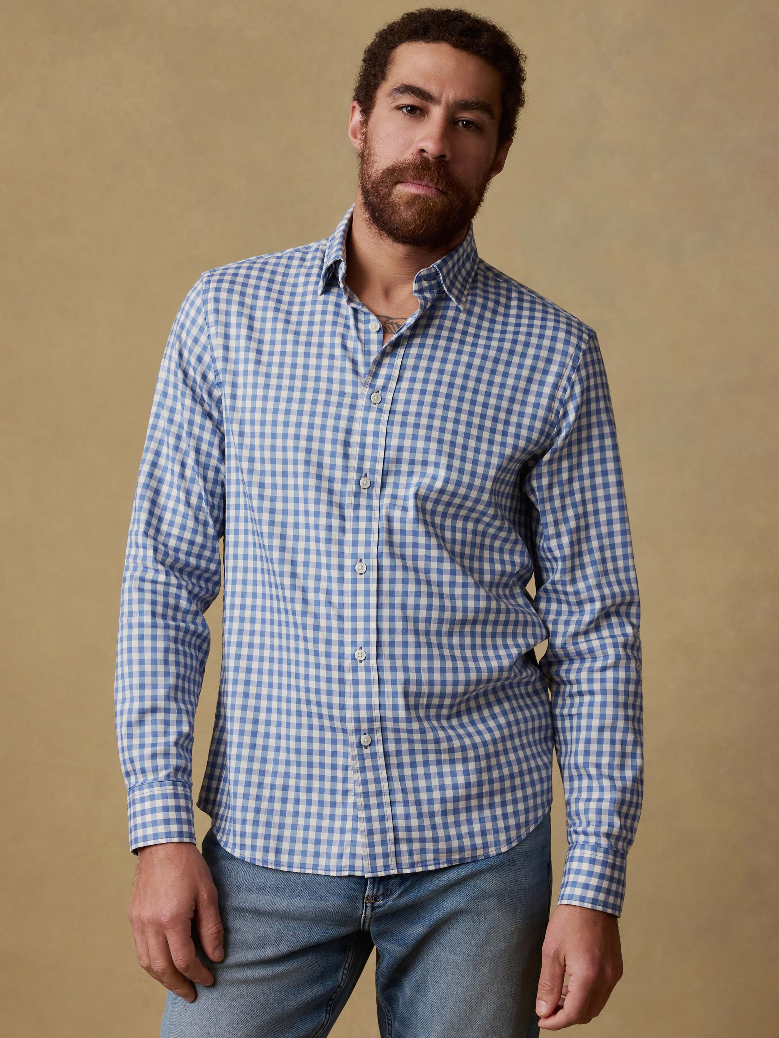 Man wearing a blue and white checkered shirt and blue jeans against a beige background