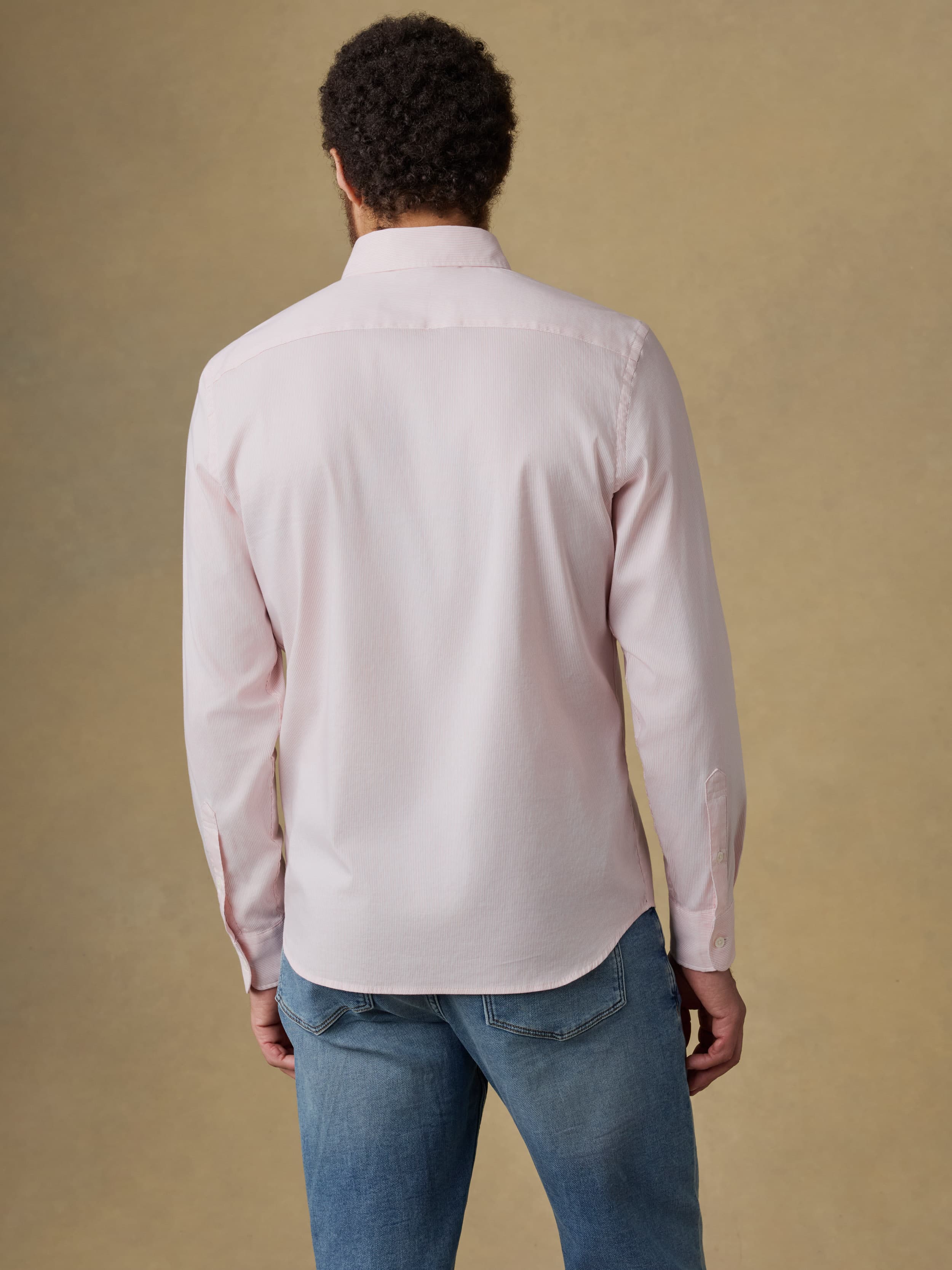 Man wearing a light pink shirt and blue jeans against a beige background