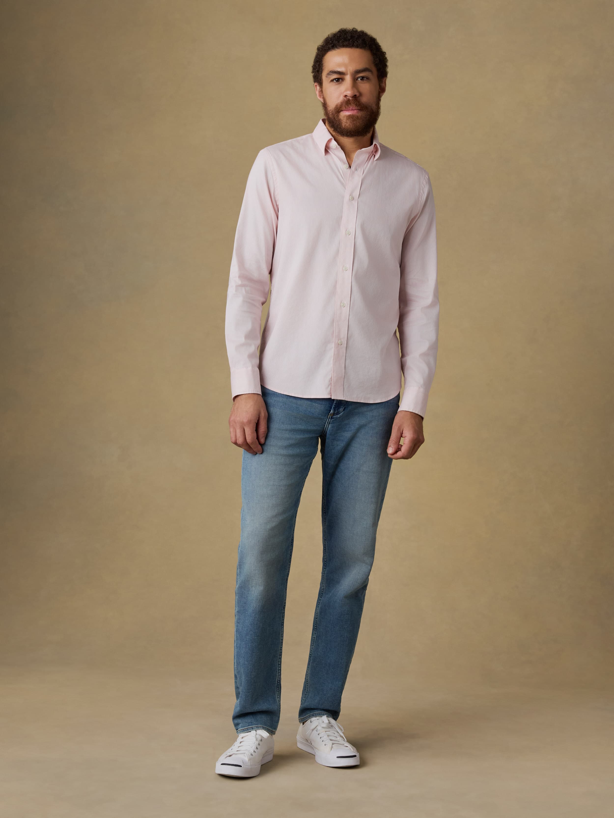 Man wearing a light pink shirt and blue jeans against a beige background