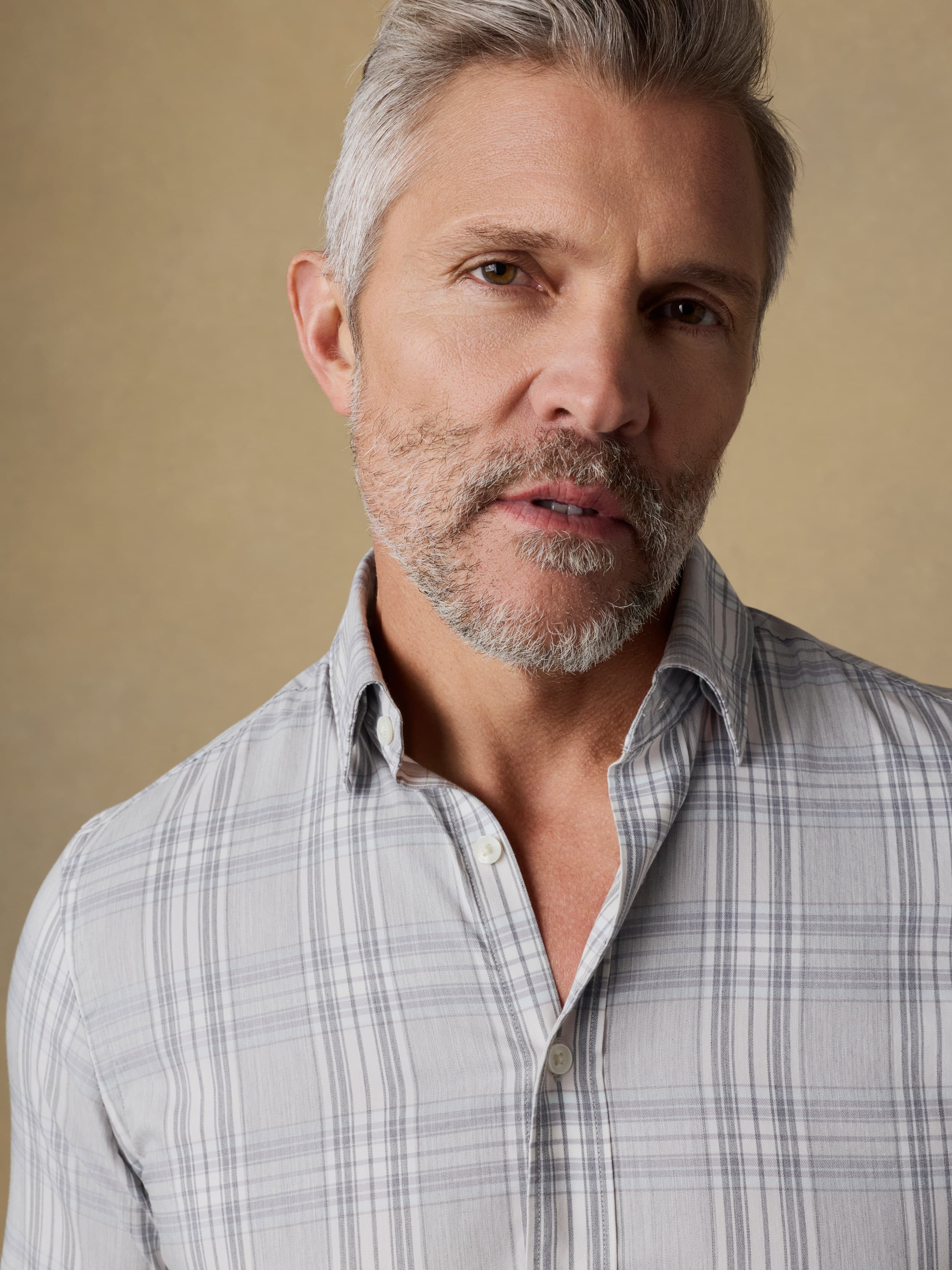 Close up shot of a man wearing a gray plaid shirt against a beige background