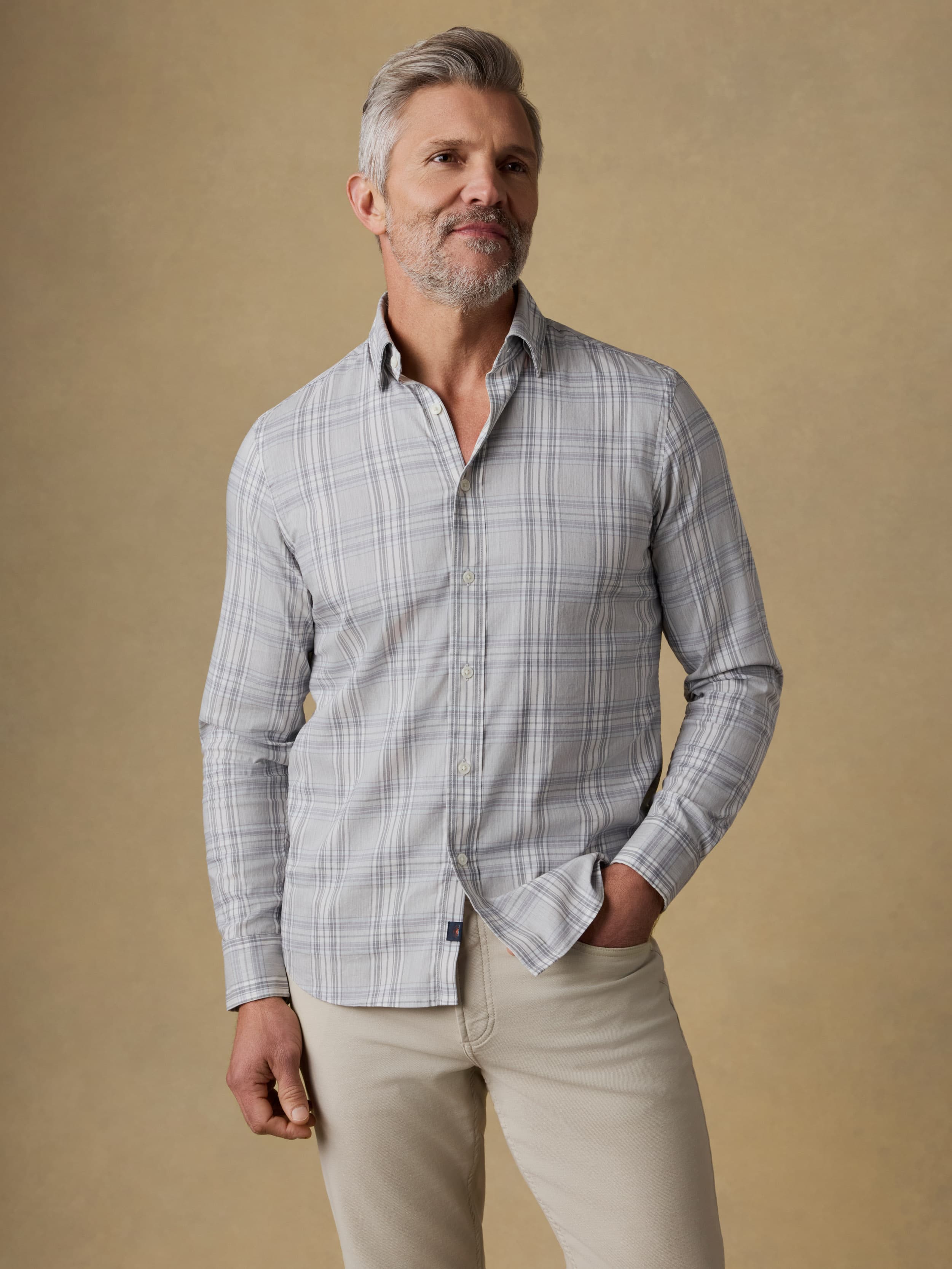 Man wearing a gray plaid shirt and beige pants against a beige background