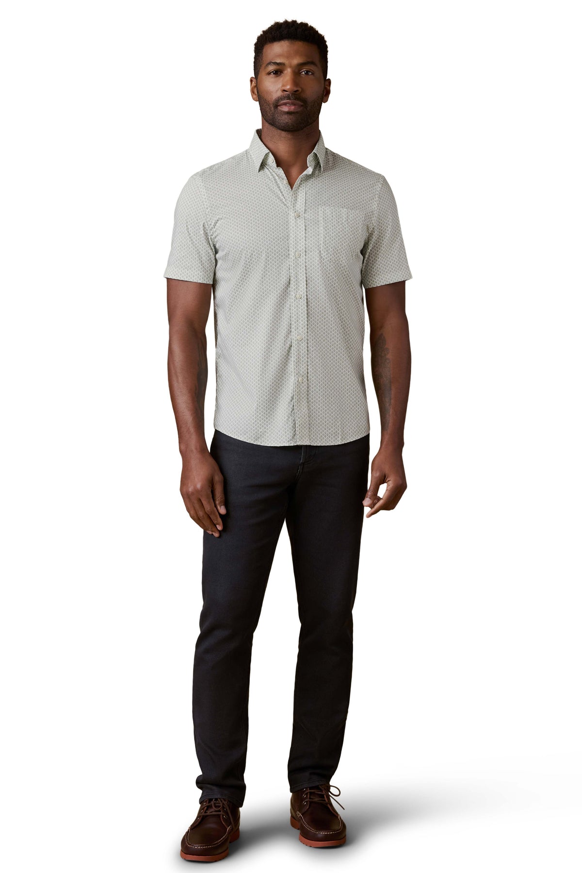 A man wearing a green printed shirt, black jeans, and brown shoes, image 2 of 3