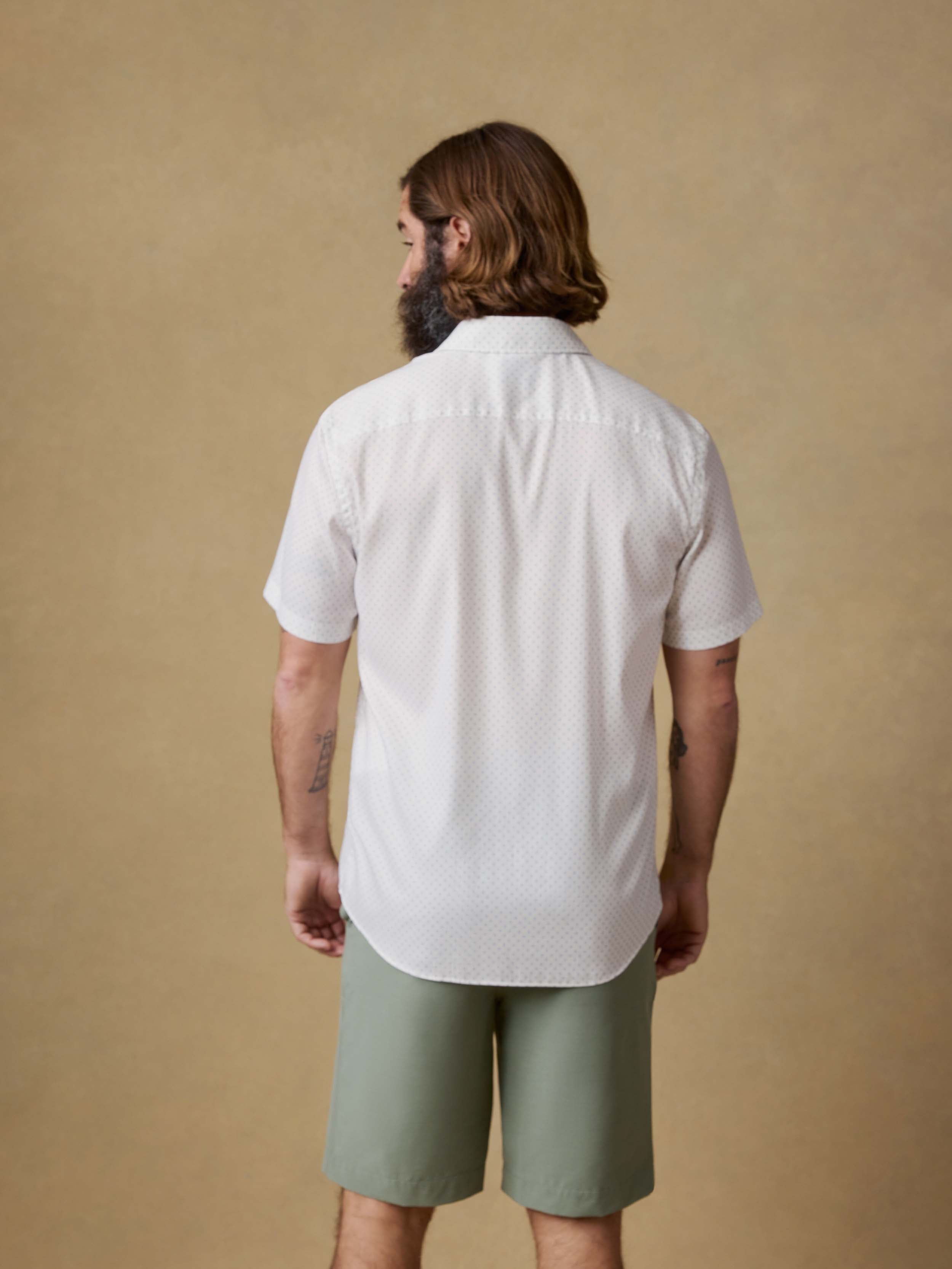 Back view of a man wearing a white short-sleeve shirt and green shorts against a beige background