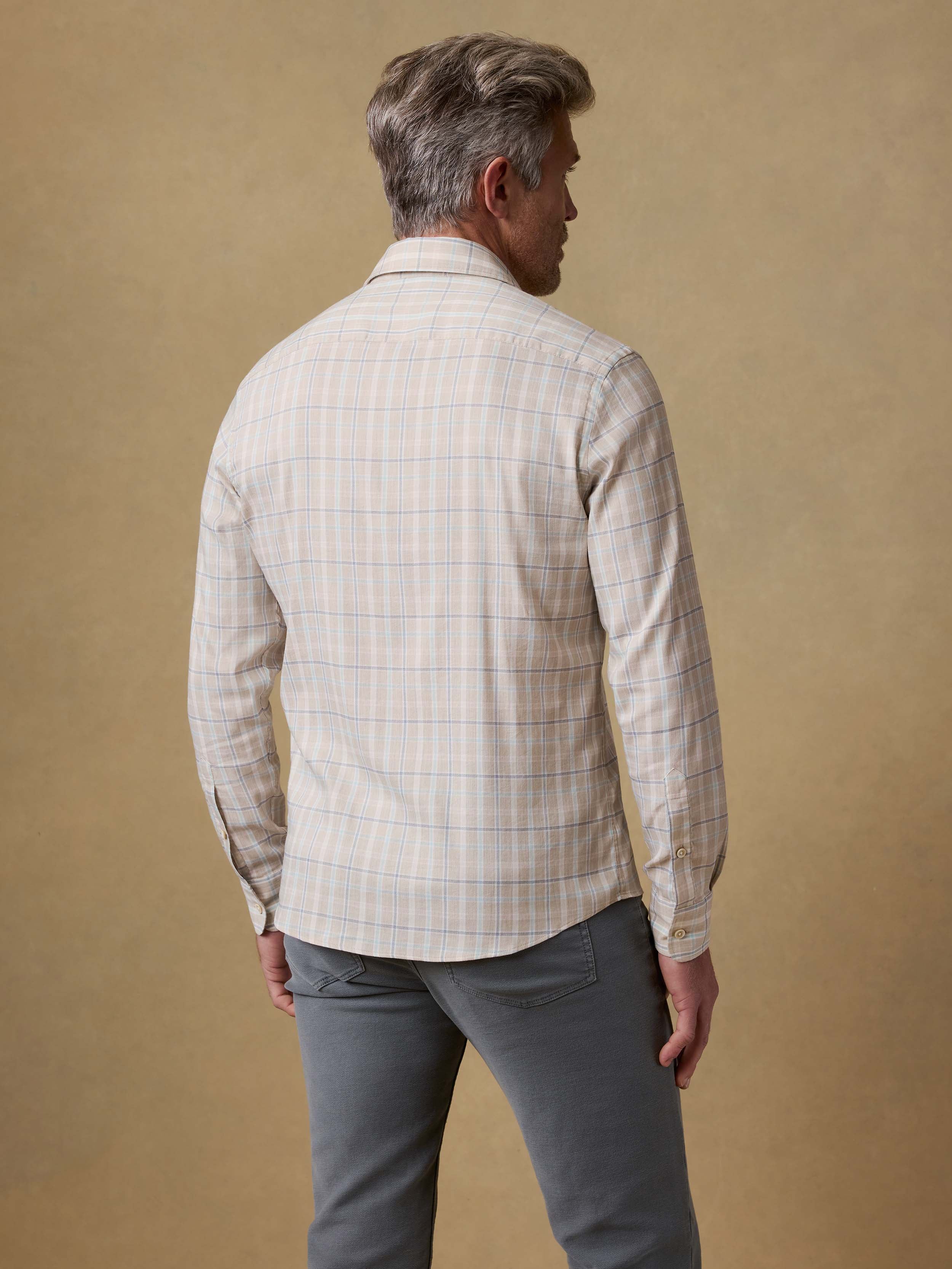 Back view of a man wearing a light-colored plaid shirt against a beige background